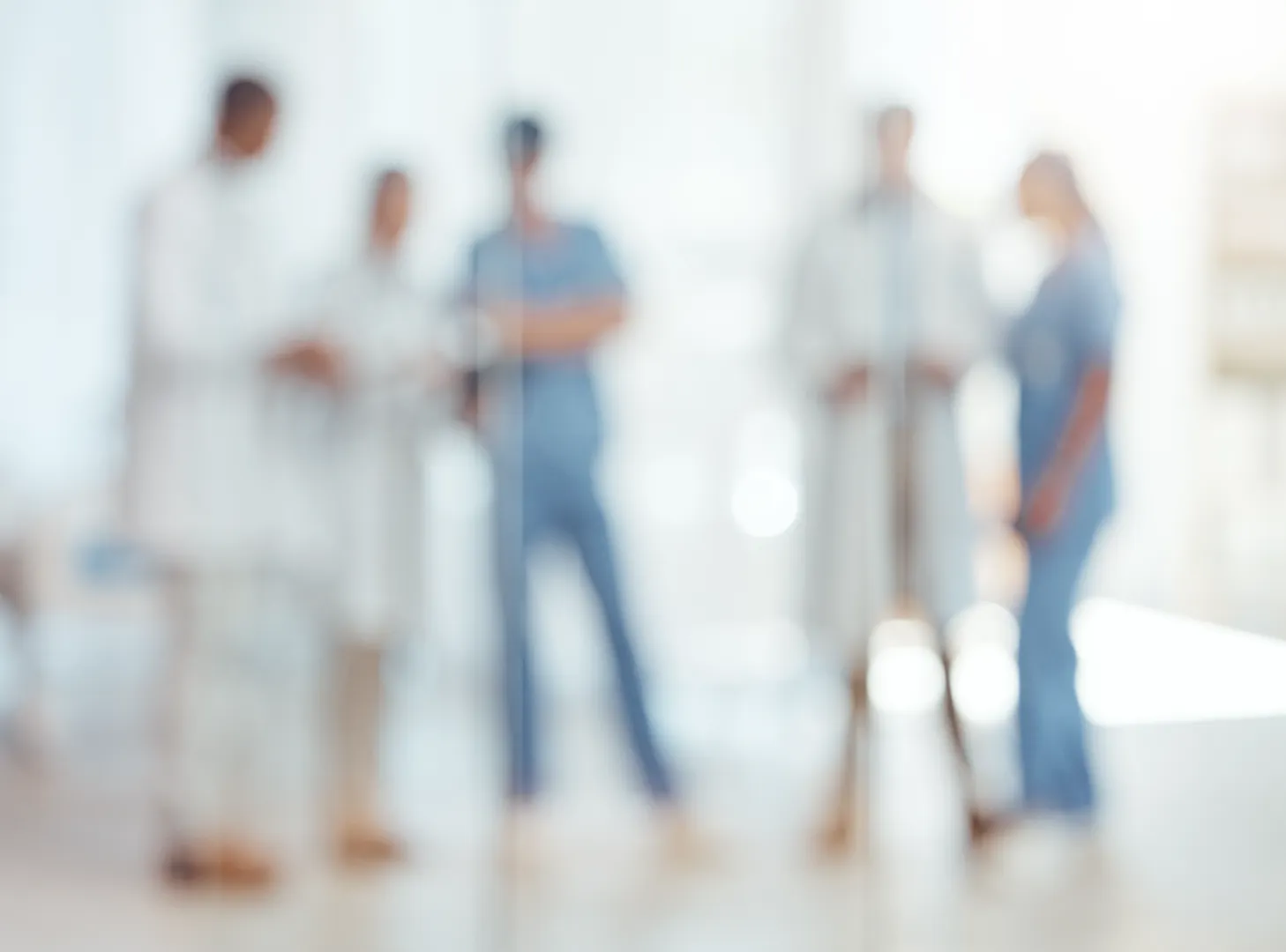 Blurred image of five medical professionals standing and discussing in a bright room.