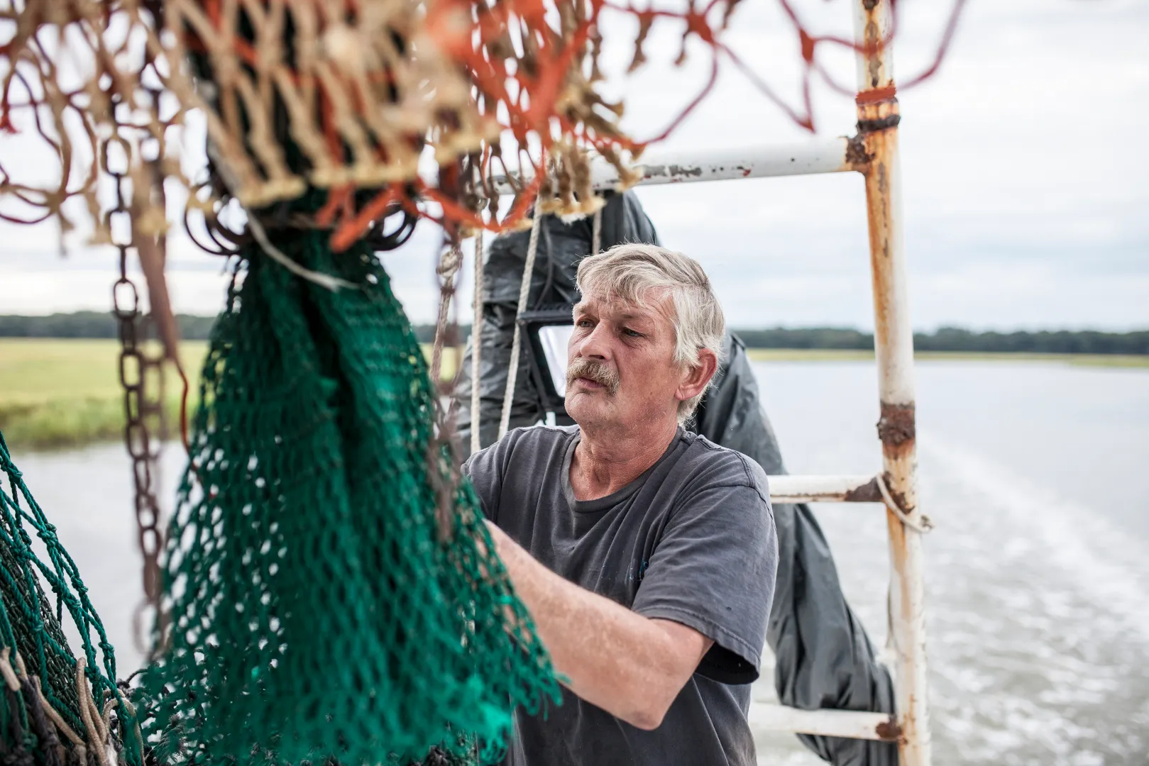 Fishing boat crewman working with green nets on a boat in a river or coastal waterway.