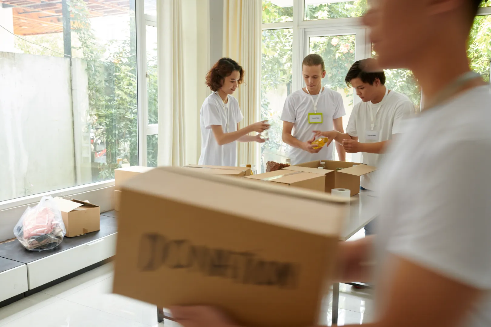 Volunteers in white shirts packing donation boxes in a bright room with large windows.
