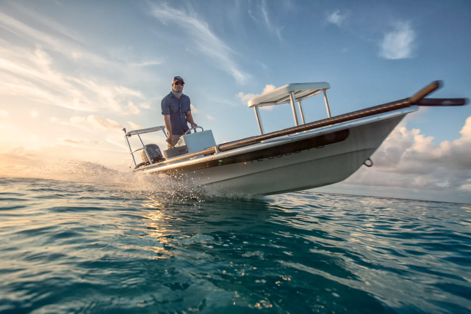 Man steering a small motorboat speeding over ocean water during a clear sky sunset.