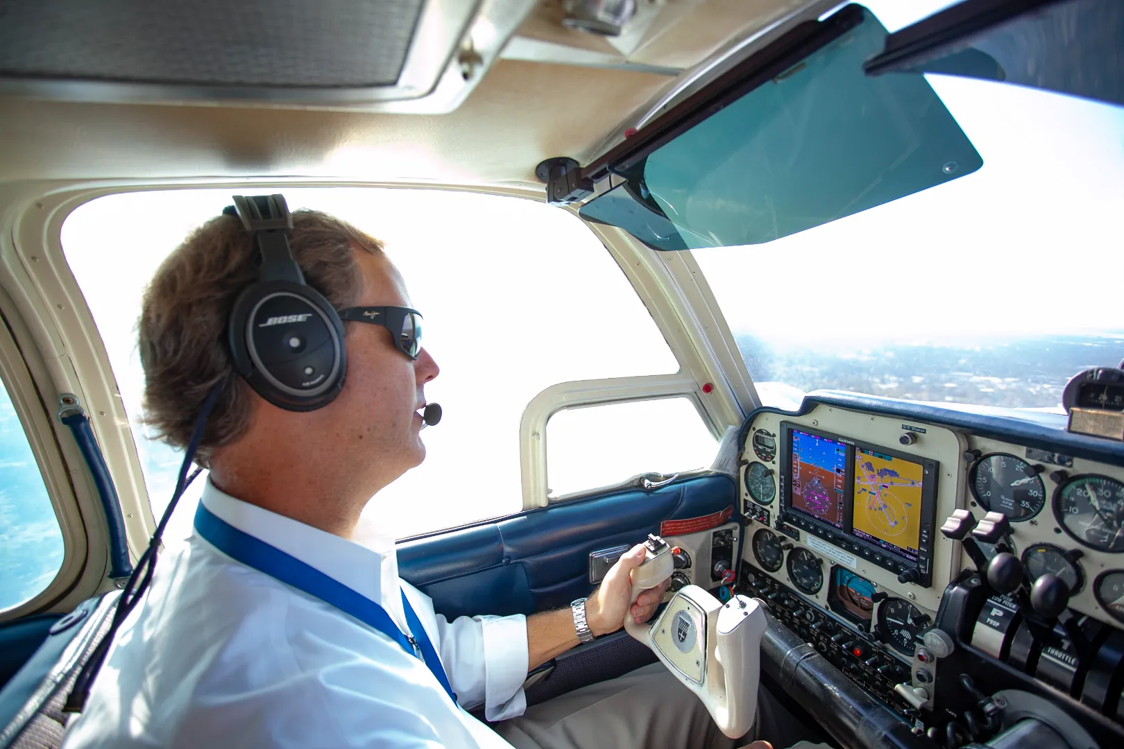 Pilot wearing headset and sunglasses operating controls inside a small airplane cockpit.