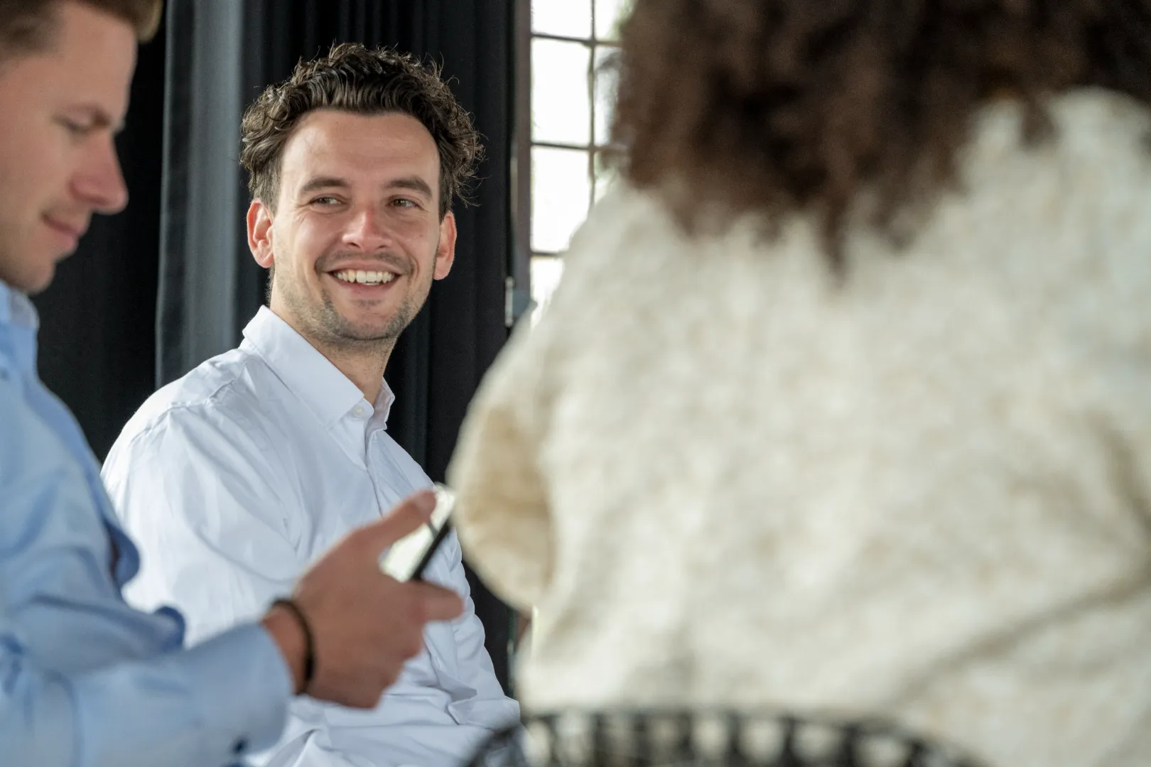 Smiling man in white shirt looking at a person in a white sweater during a meeting.