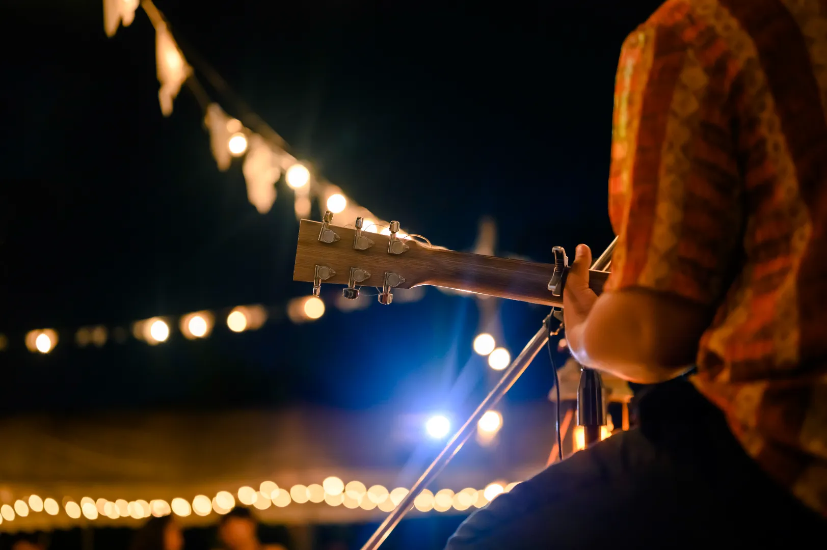 Person playing acoustic guitar with string lights glowing in the background at night.