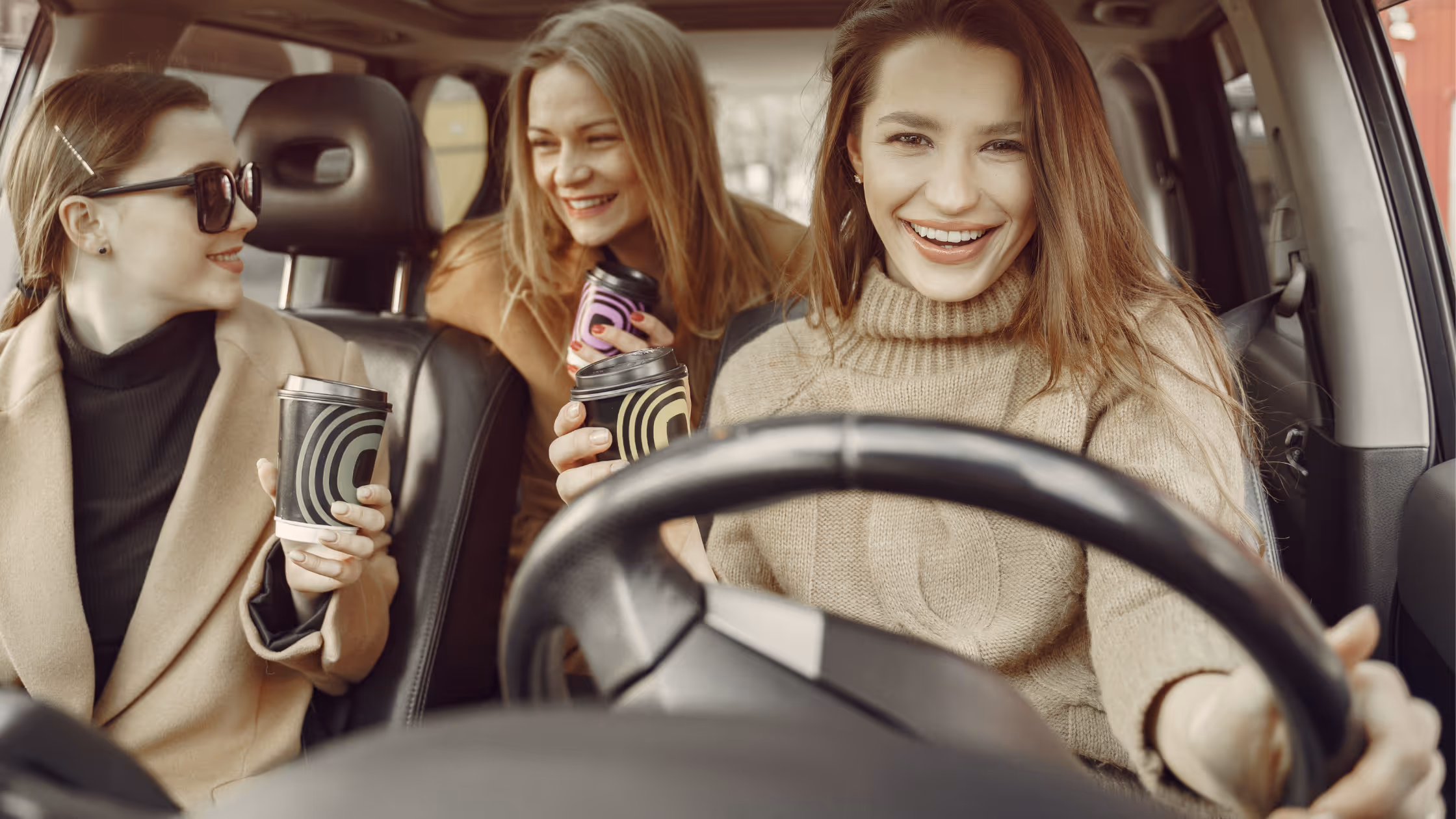 Three women holding coffee in a car