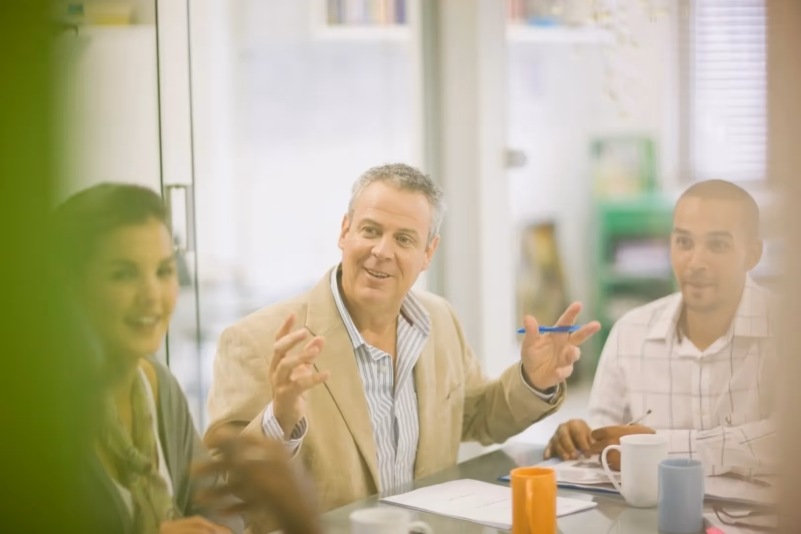 A photograph of three people having a conversation while sat at an office conference table