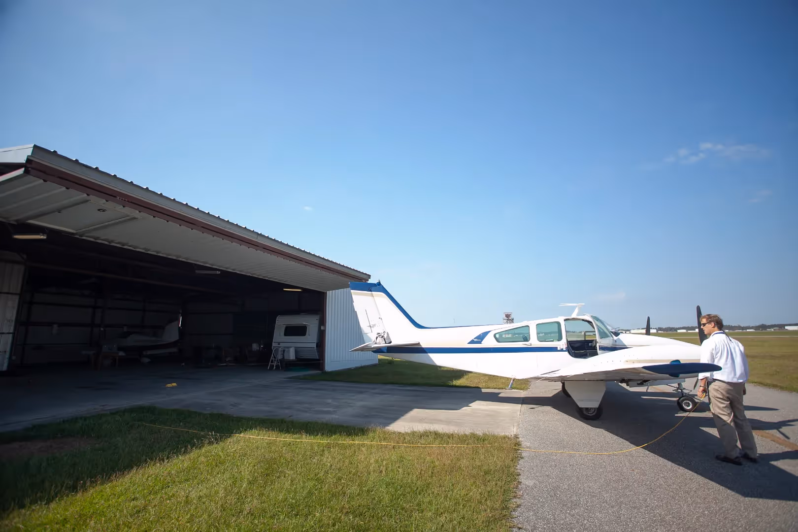 A photograph of a man and a small prop plane outside of a hangar
