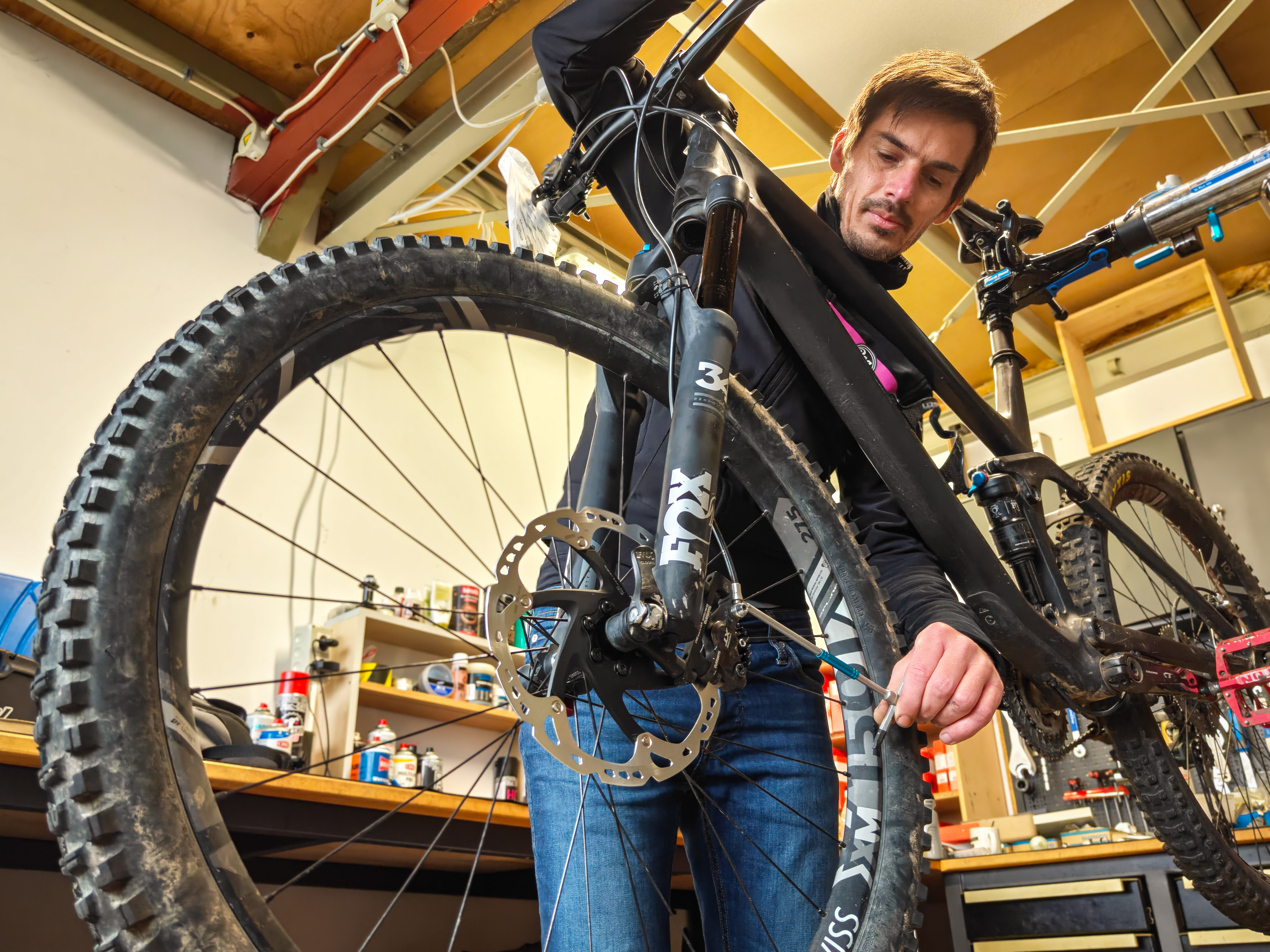 Man repairing the front wheel of a mountain bike indoors in a workshop setting.