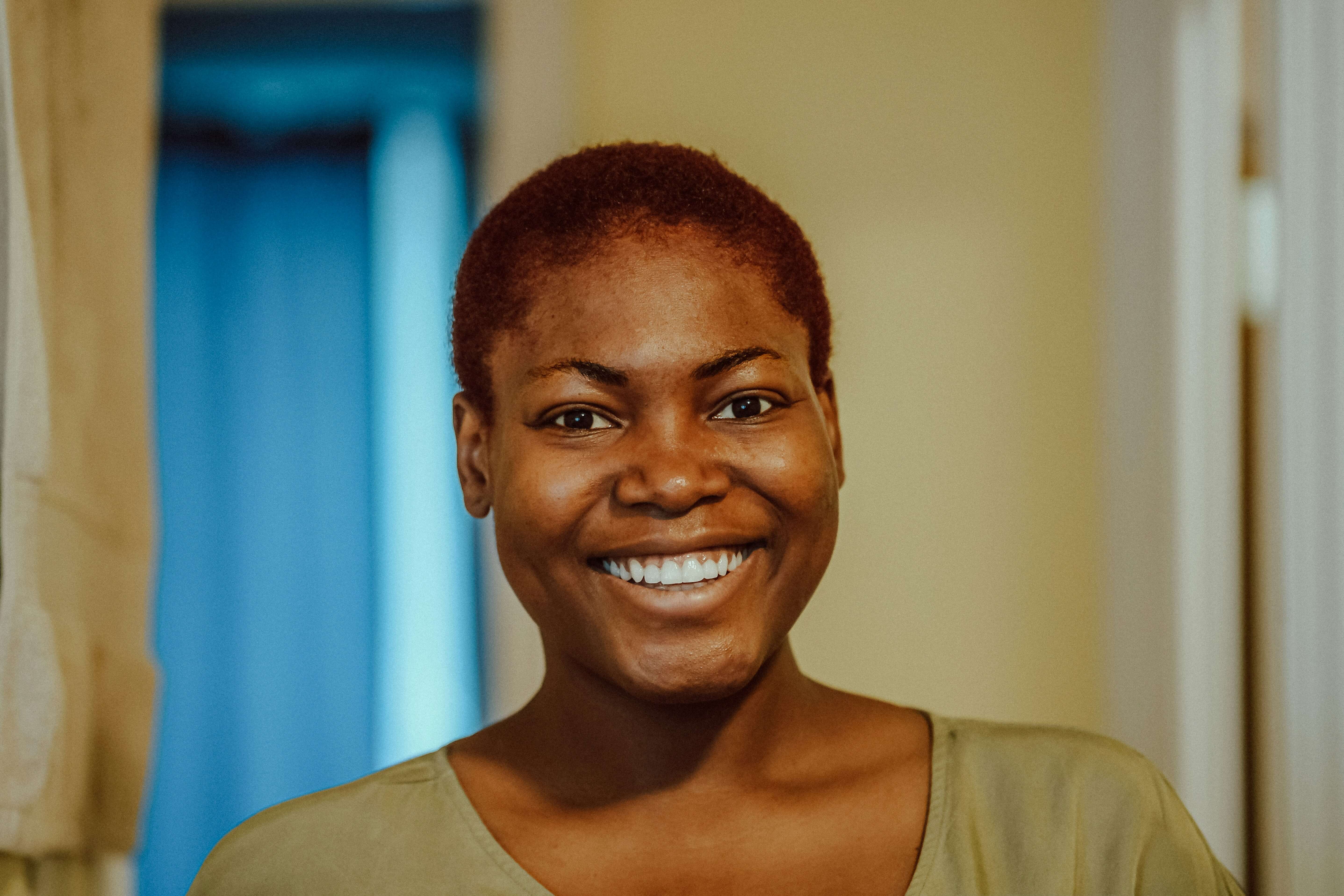 Smiling person with short reddish hair wearing a green shirt standing indoors with a blue curtain in the background.