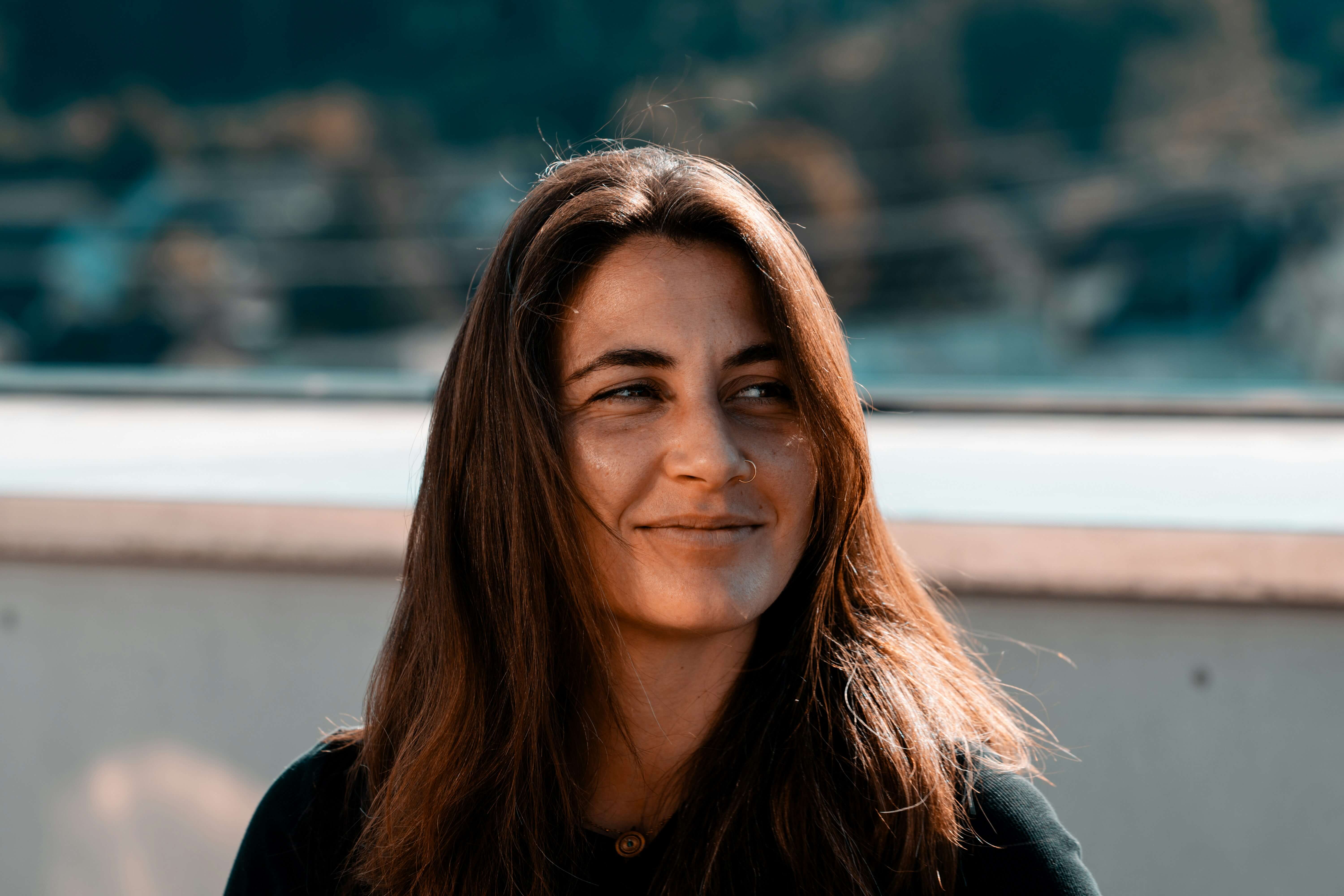 Smiling woman with long brown hair looking to the side outdoors in natural light.