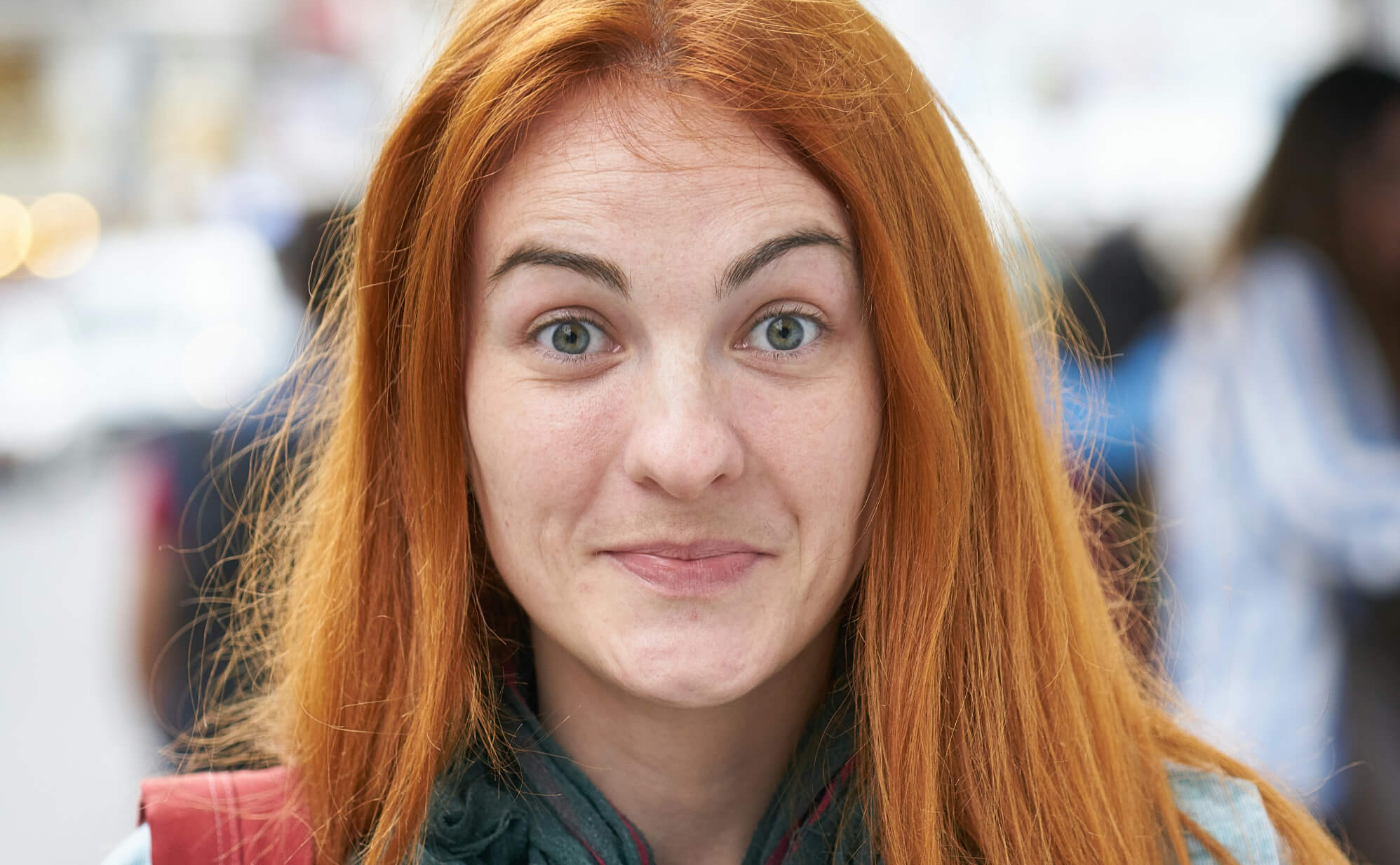 Close-up of a woman with long red hair and green eyes smiling slightly in an outdoor setting.