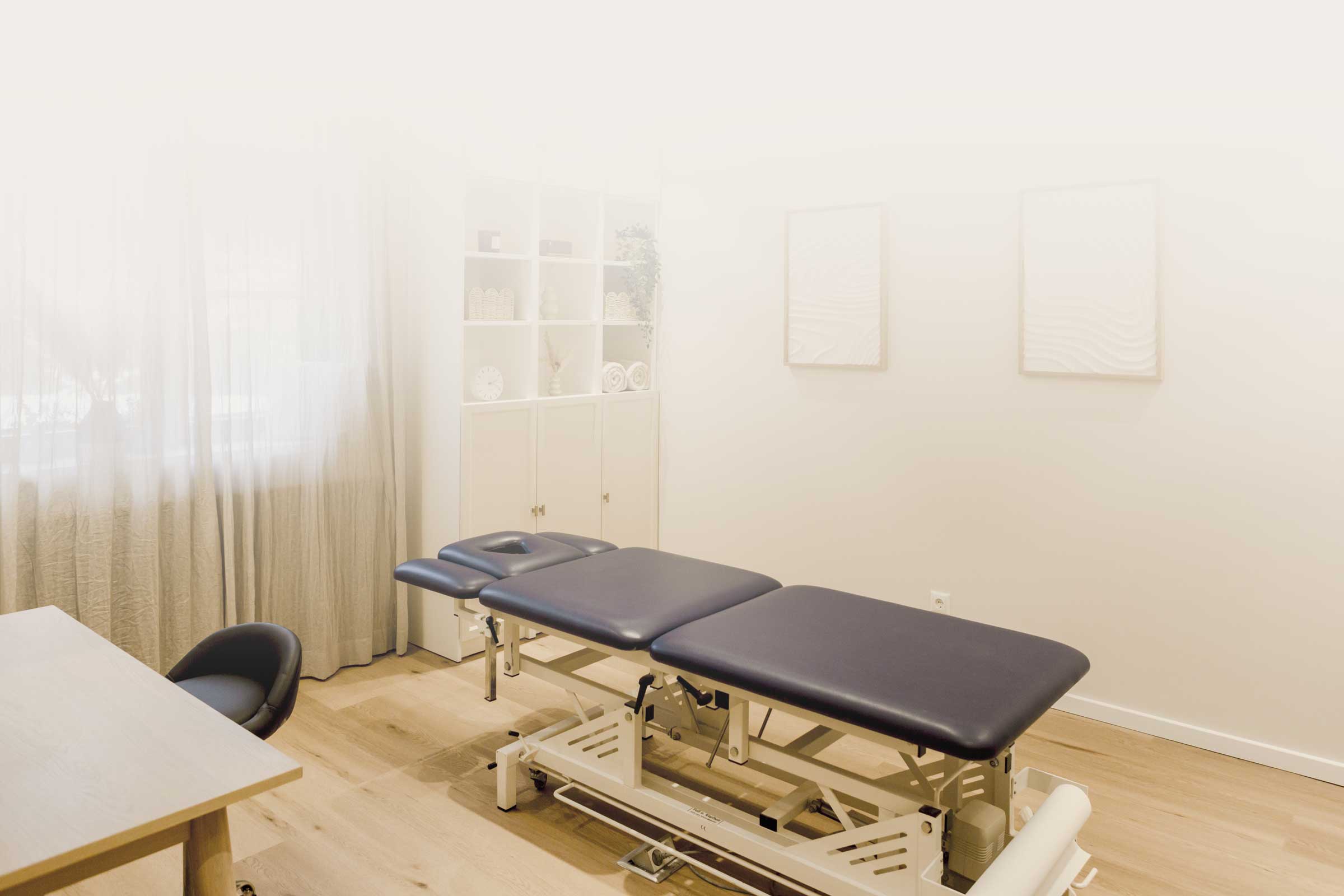 Warmer Praxisraum mit Liege und viel Licht durch großes Fenster