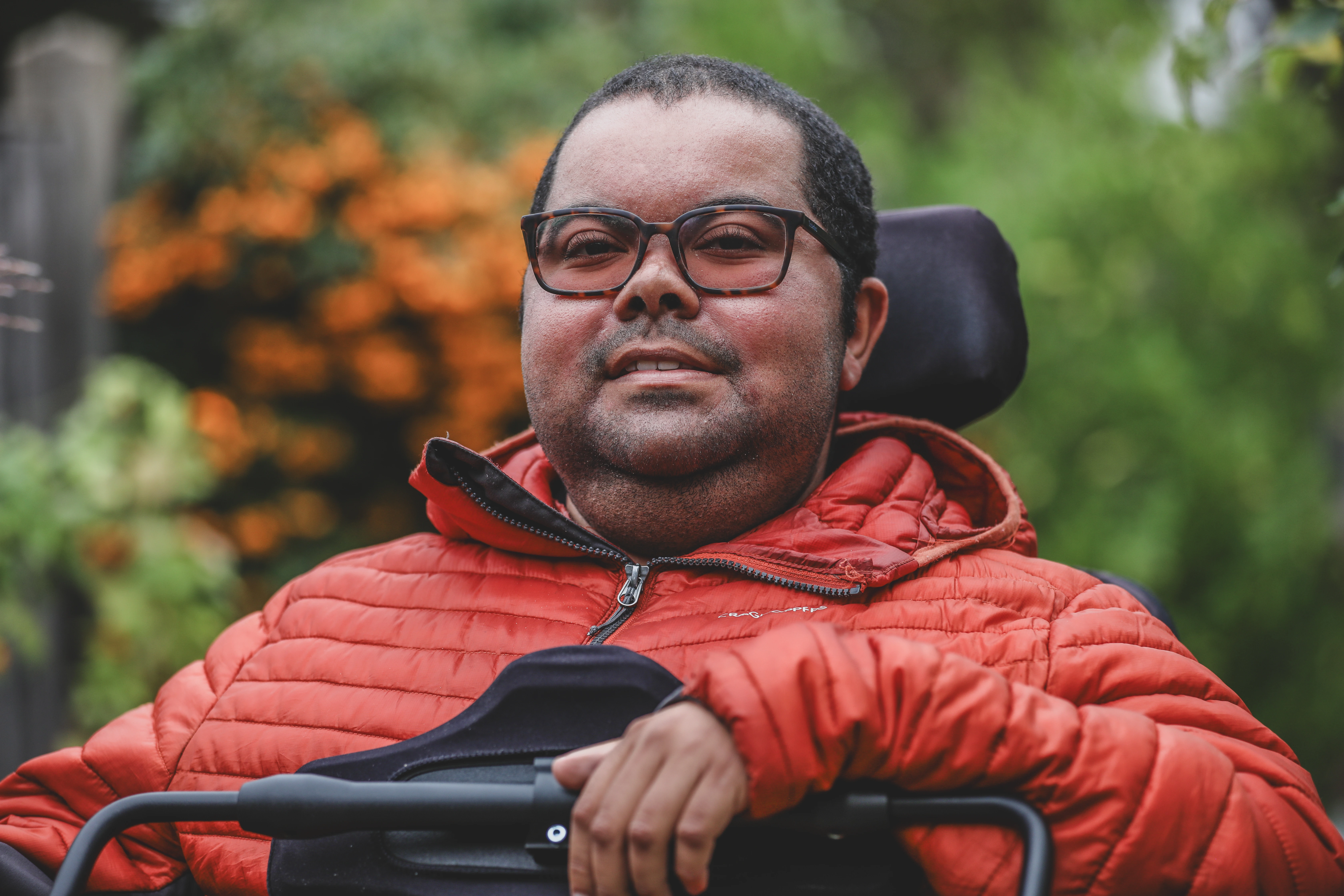 Man in glasses and orange jacket smiling in a garden
