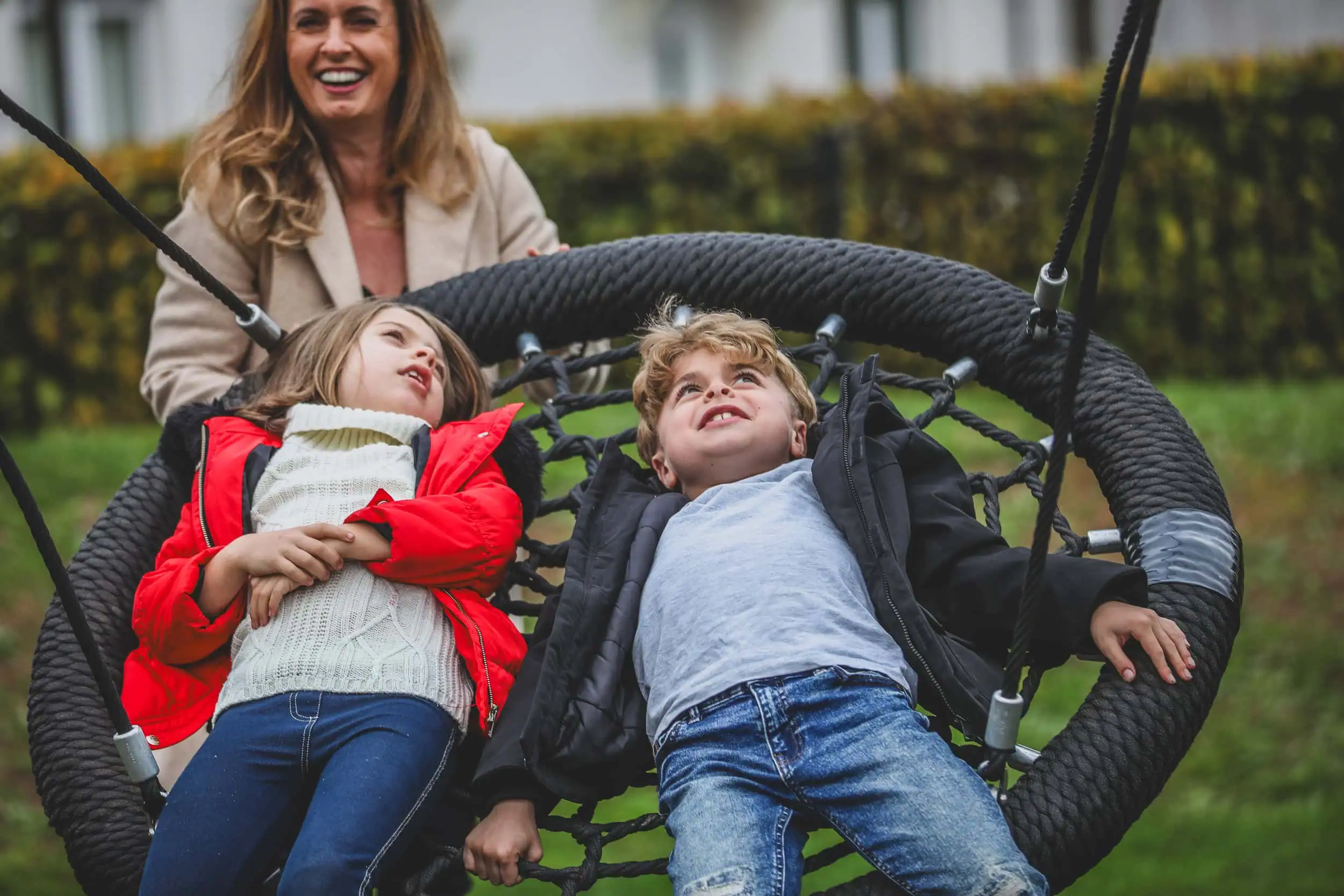 Family laughing together while playing on a swing in the park