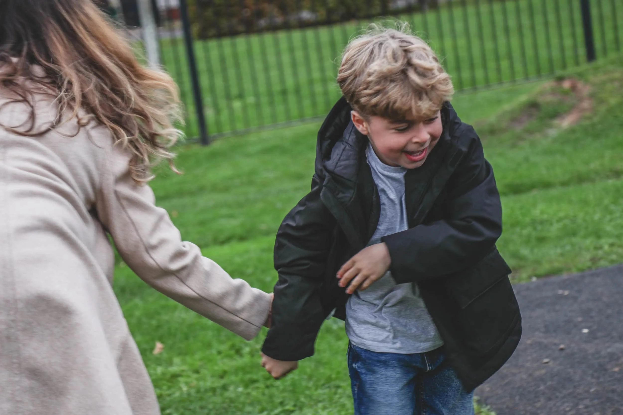 Woman and boy playing together outdoors, boy laughing while running in park