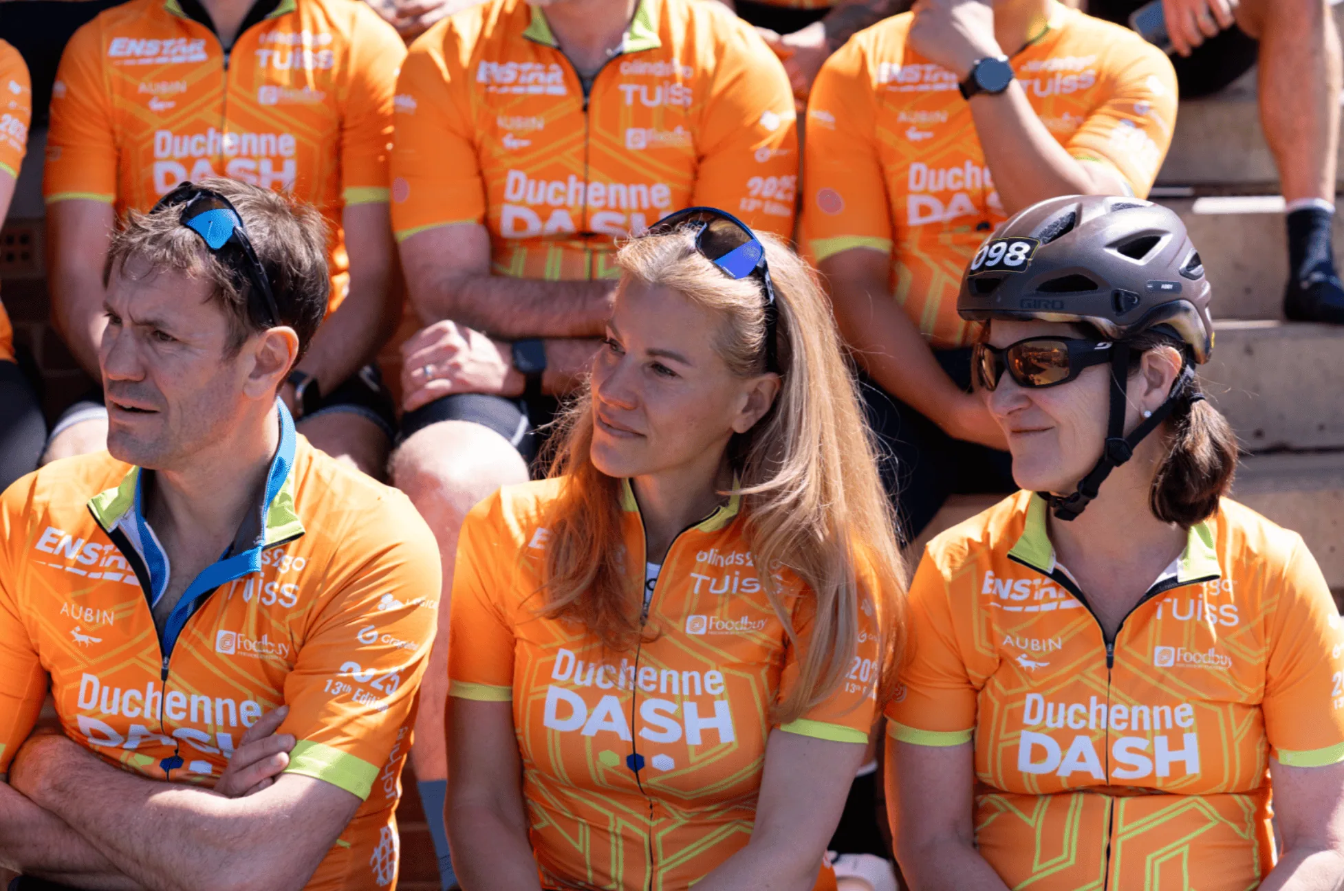 Three cyclists in orange Duchenne DASH jerseys sitting together at event