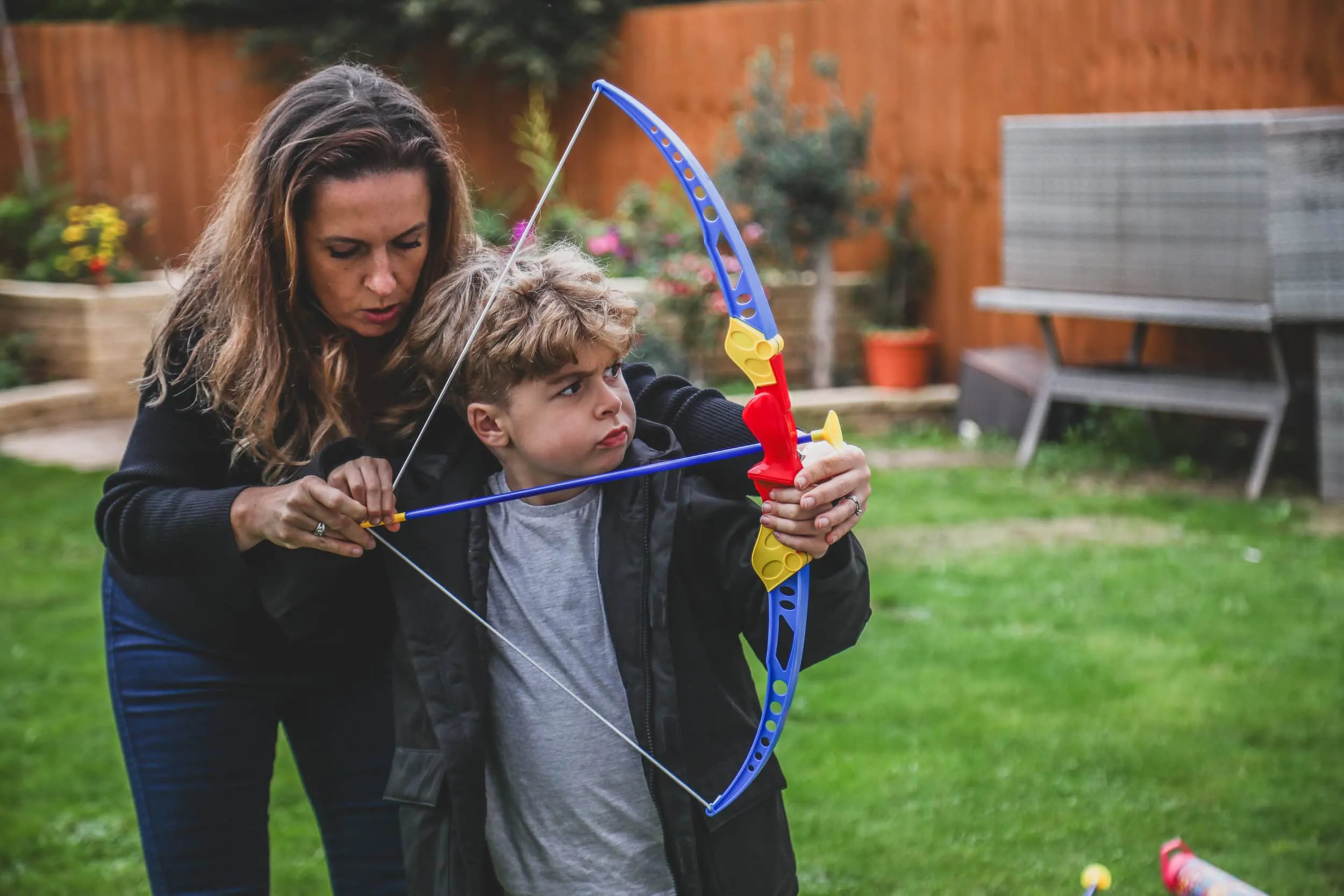 Woman and boy playing with toy archery set in backyard