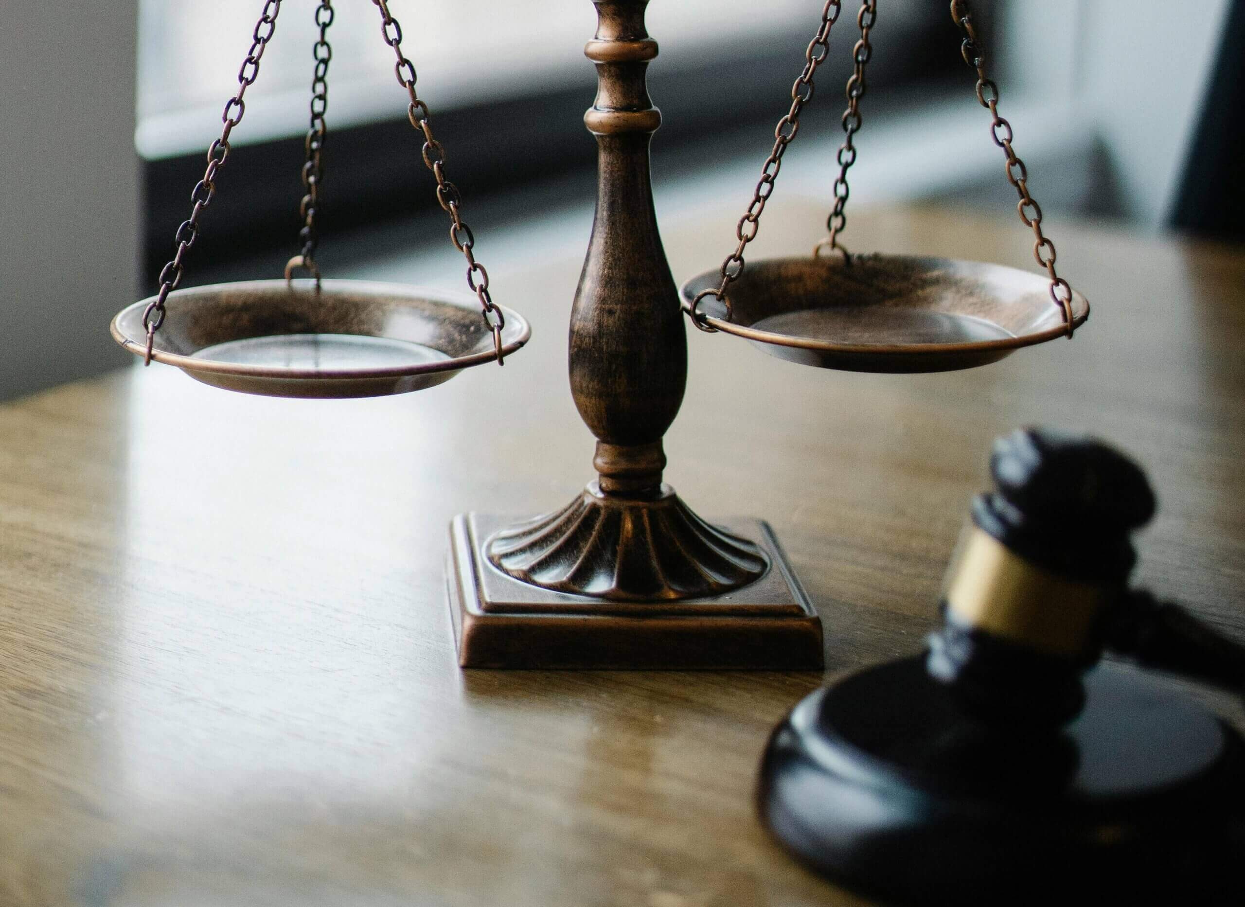 Close-up of a wooden balance scale and a judge's gavel on a wooden table.