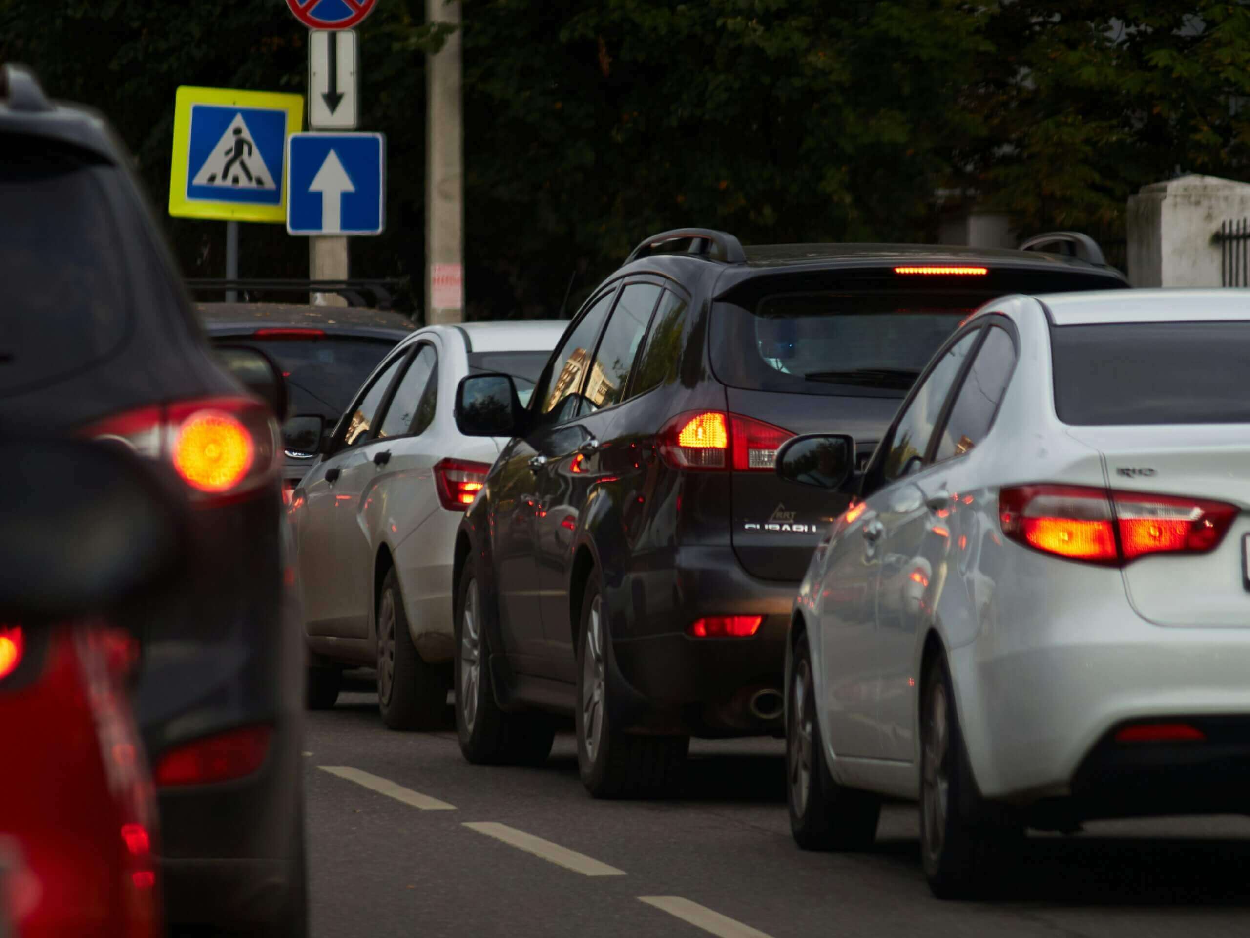 A line of cars with brake lights on in a traffic jam on a city street near traffic signs.