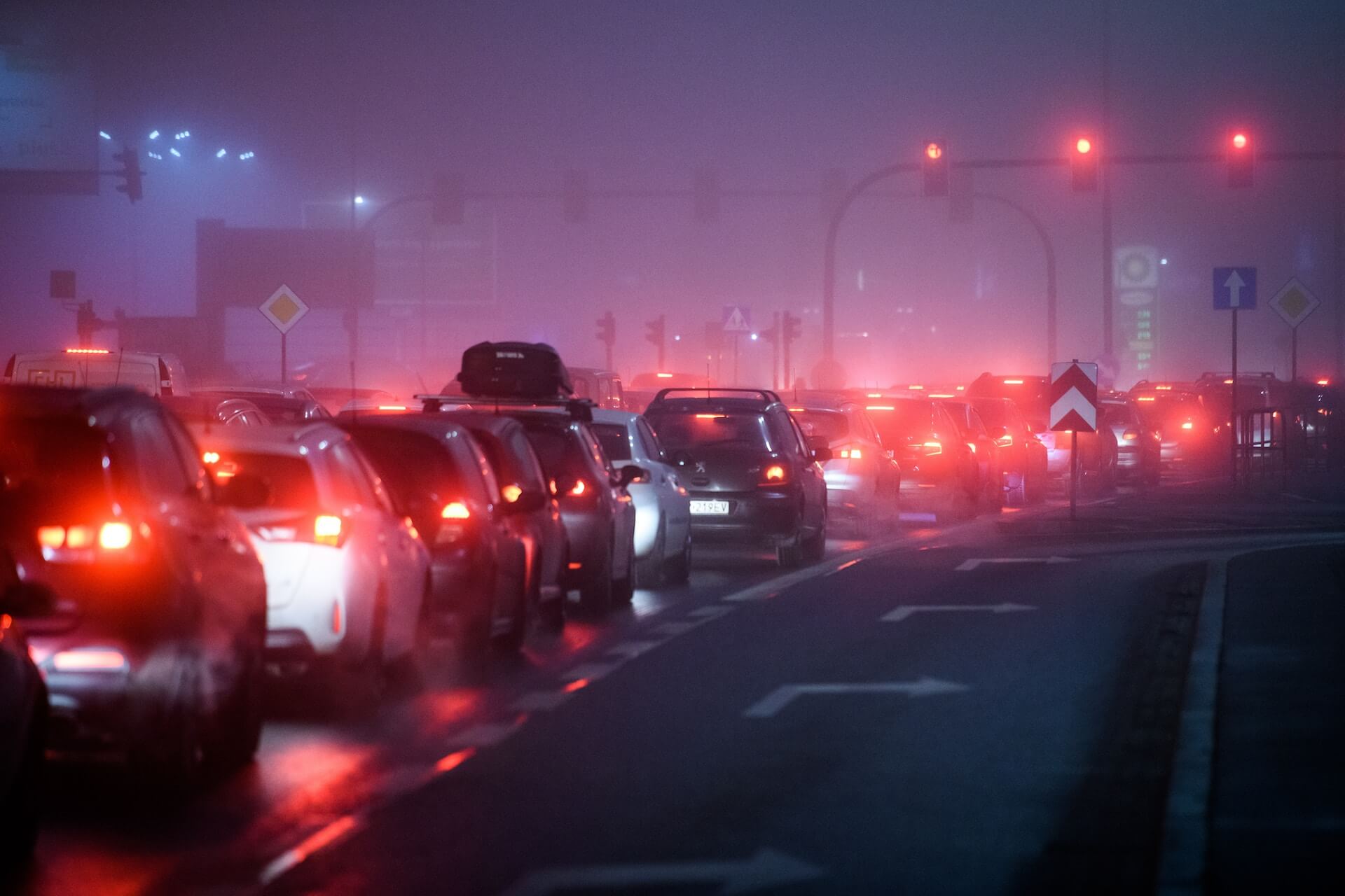 Heavy traffic with many cars stopped at a red light on a foggy night, with red brake lights illuminating the scene.
