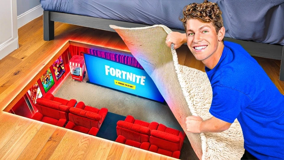 A man in a blue shirt lifts a carpet on a wooden floor to reveal a hidden home theater with red couches and a large screen displaying the Fortnite game start screen.