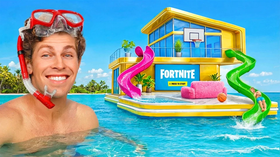 A man wearing a red snorkeling mask and snorkel smiling in the water next to a floating yellow house with large glass windows, a basketball hoop, two slides—pink and green—and a pink fuzzy couch with a basketball, set on a clear blue ocean under a bright sky.