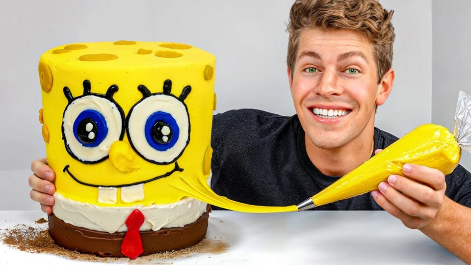 A man with light brown hair and green eyes smiles while holding a yellow piping bag, squeezing yellow icing onto a cake shaped and decorated like SpongeBob SquarePants.