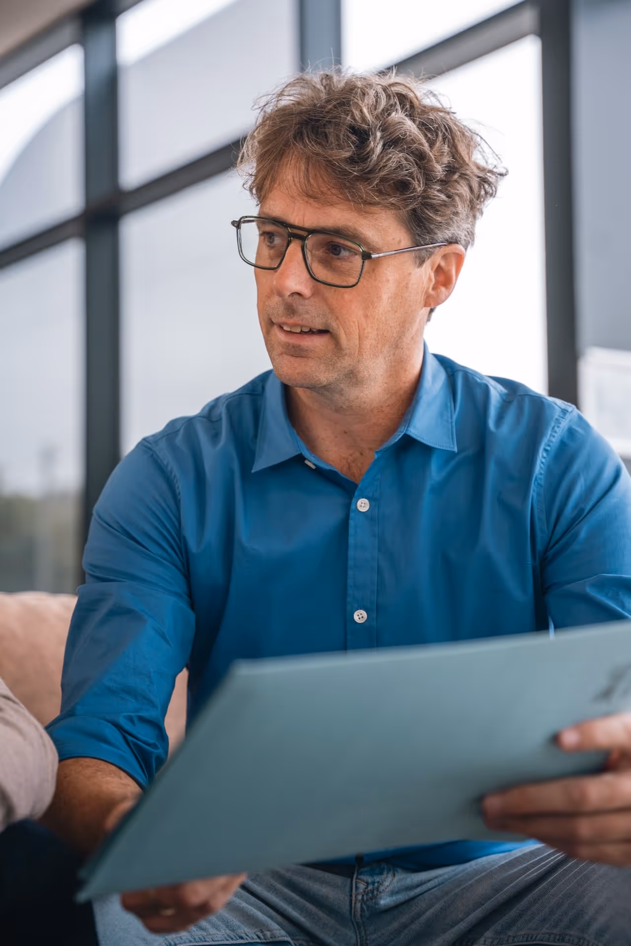 Tom, zaakvoerder van Common Sense, draagt een blauw hemd, bril, houdt een blad in de hand dat hij toont aan iemand die naast hem zit.