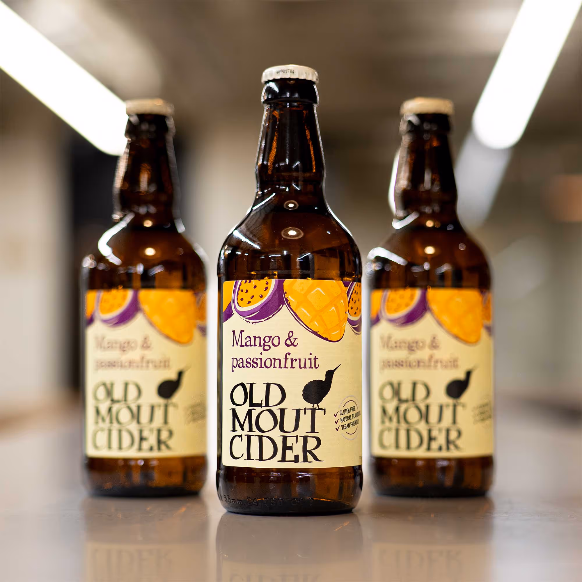  Three bottles of Old Mout Cider arranged on a wooden table, showcasing their vintage labels and unique shapes