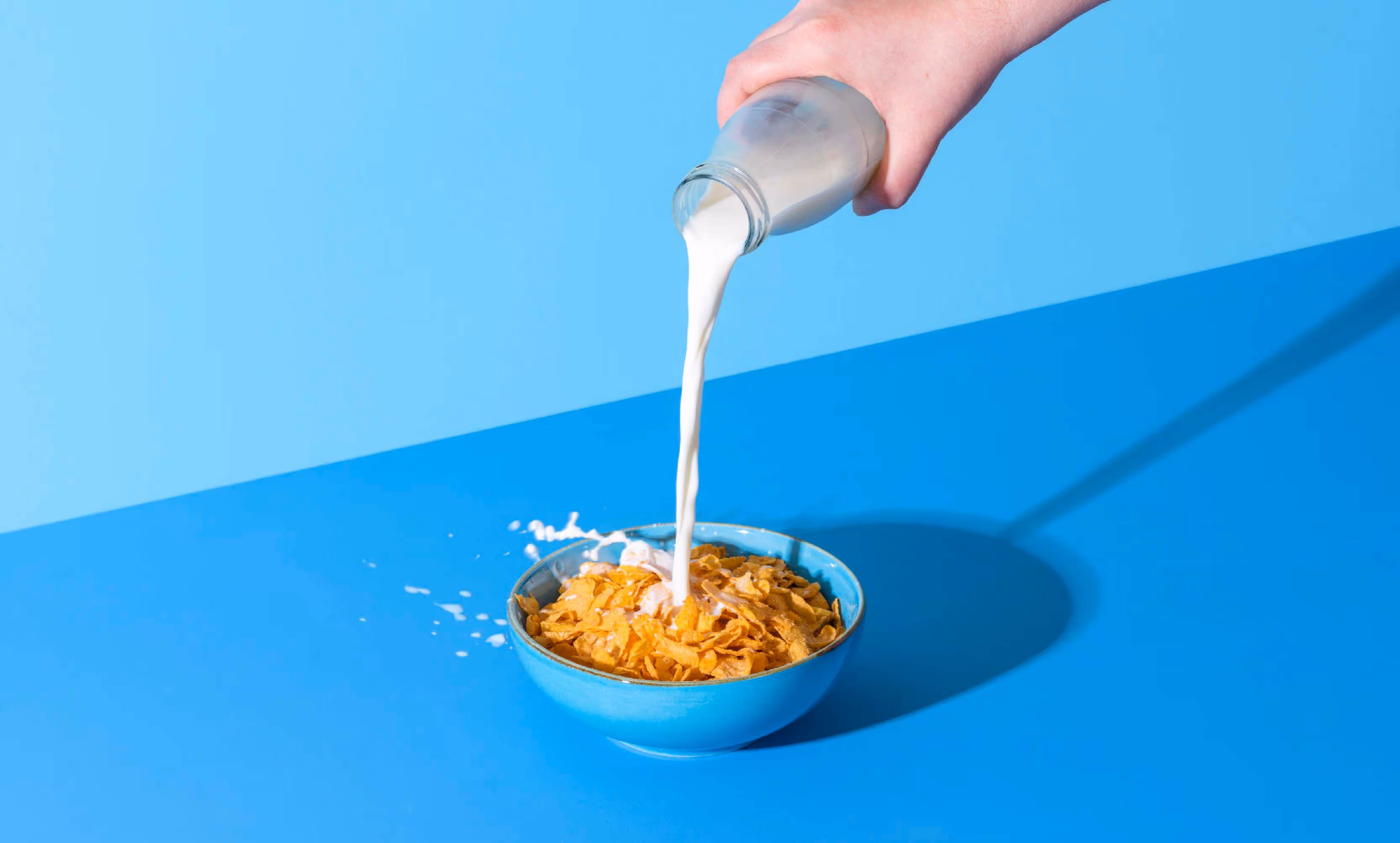 A person pouring milk into a bowl of cereal, creating a splash as the milk meets the cereal