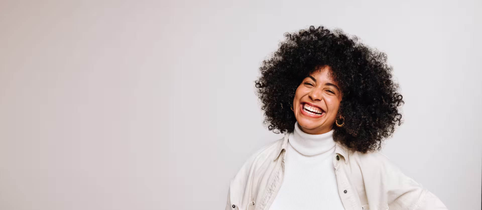 A woman with curly hair smiles warmly, showcasing her joyful expression.