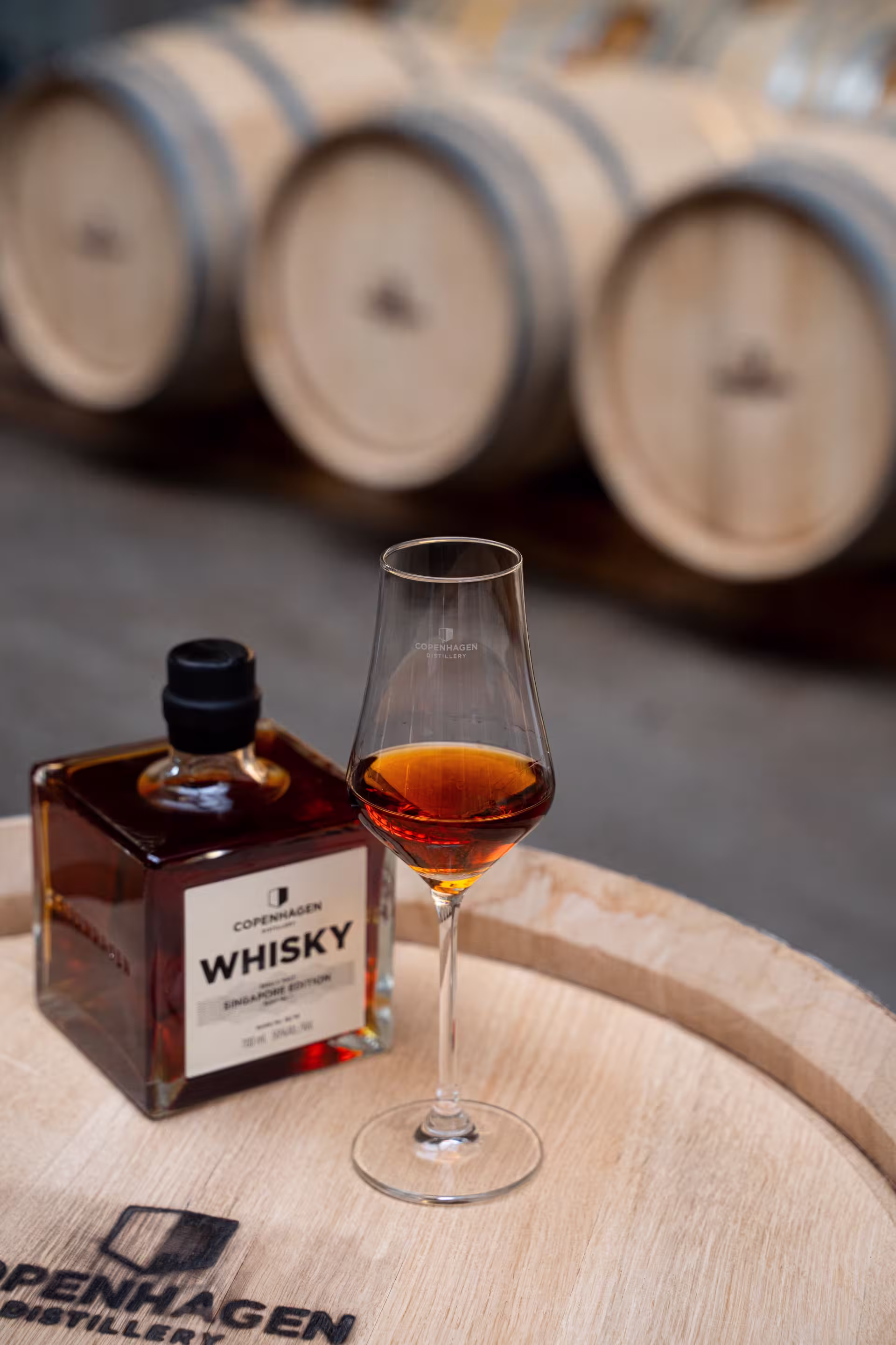 A bottle of whiskey rests on a rustic wooden barrel, showcasing its rich amber colour and elegant label.