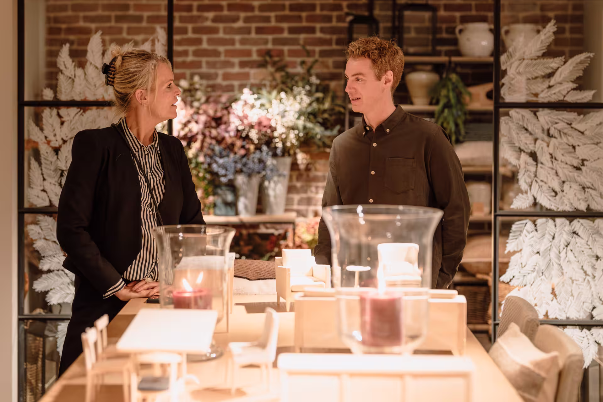 Two people standing at a table in a store, engaged in conversation while examining products.