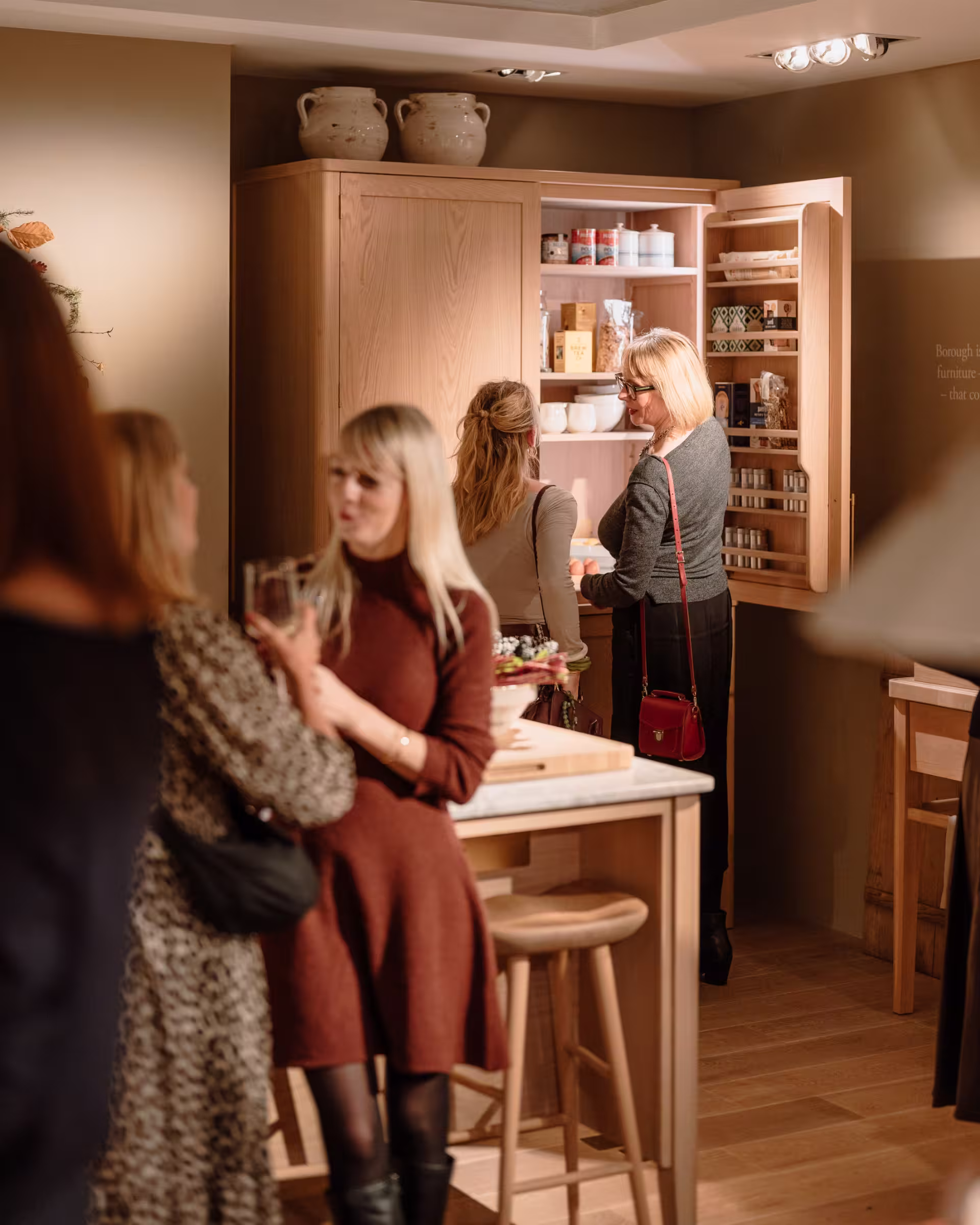 Several people standing in a kitchen, interacting and collaborating on meal preparation in a warm, inviting atmosphere.