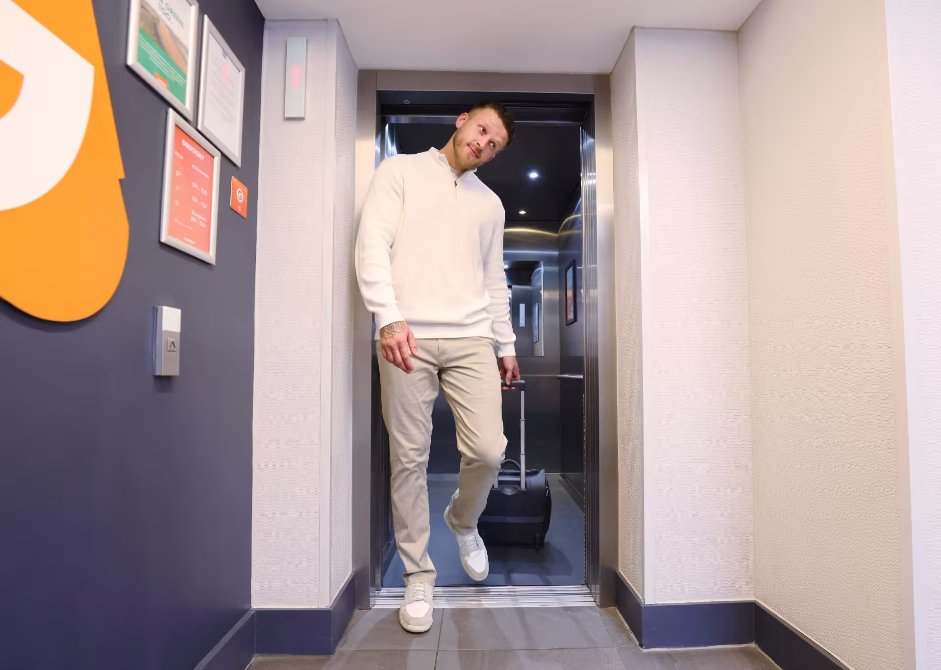 A man stands in an elevator, holding his luggage, ready to depart to his destination.