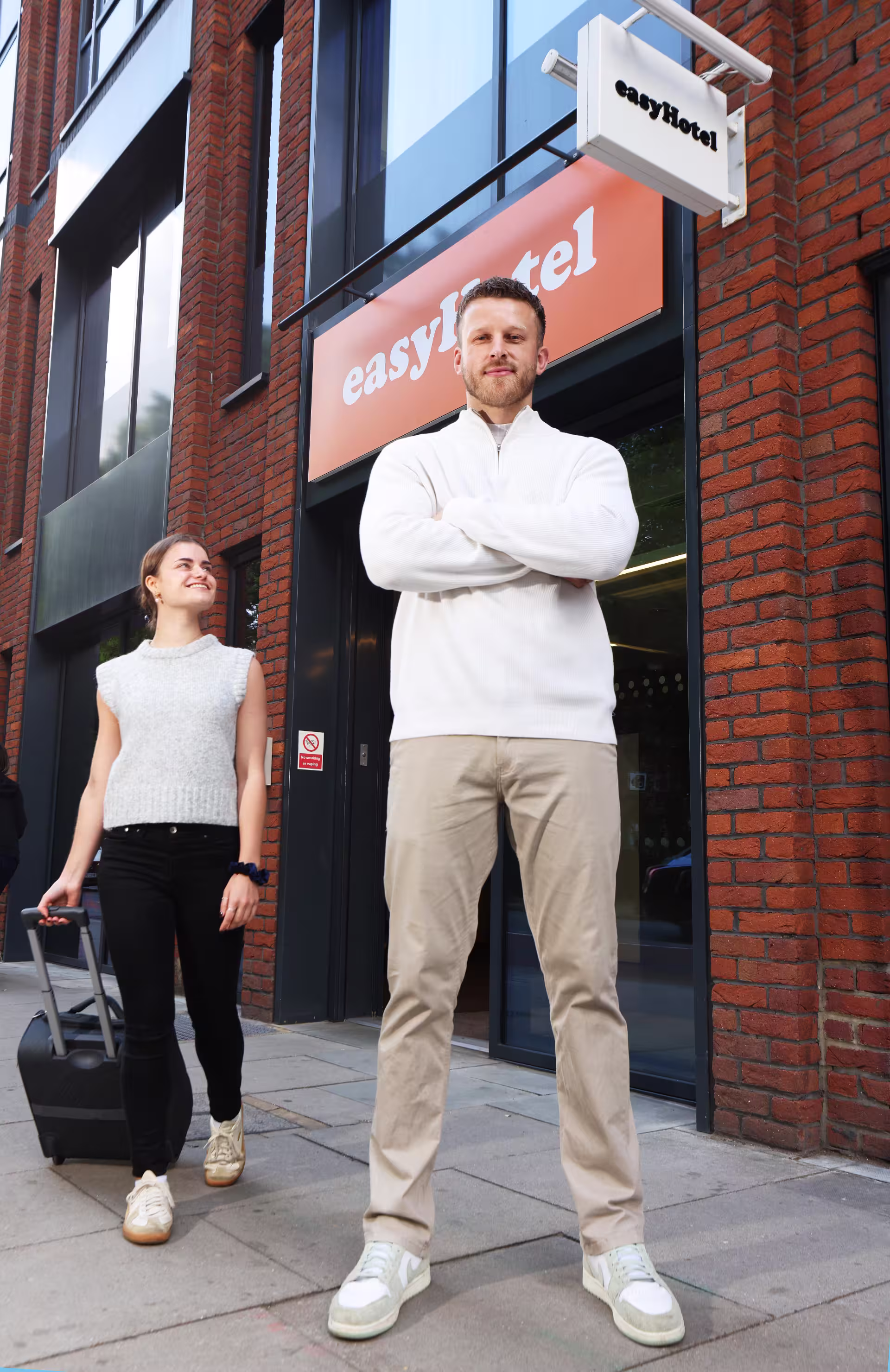 A man and a woman stand together on a sidewalk, engaged in conversation.