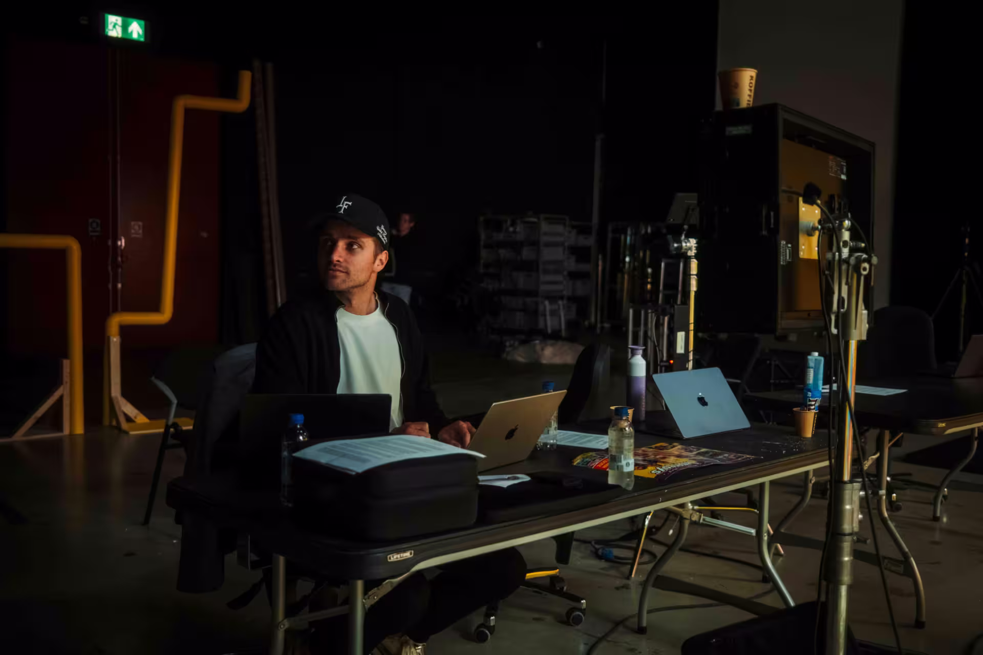 A man seated at a table, working on a laptop with a camera positioned nearby.