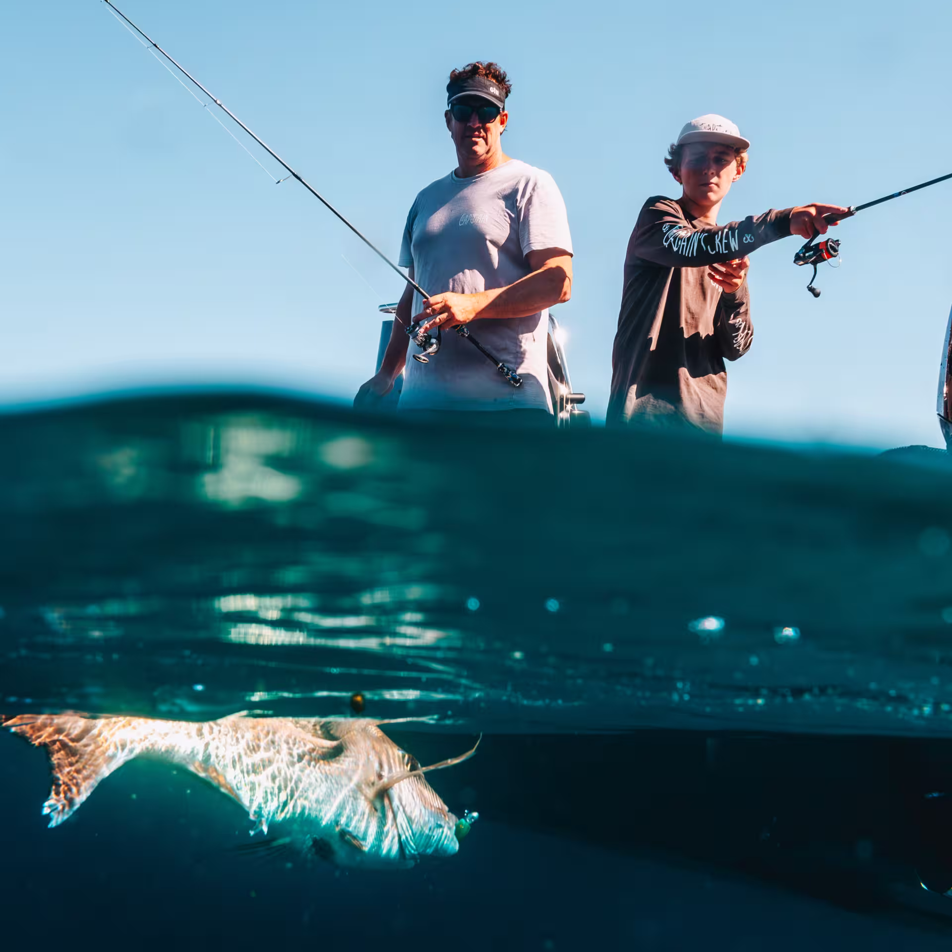 Split-level over-under water shot of two anglers fishing from a boat with a Mercury Pro XS outboard, with a fish visible just below the surface