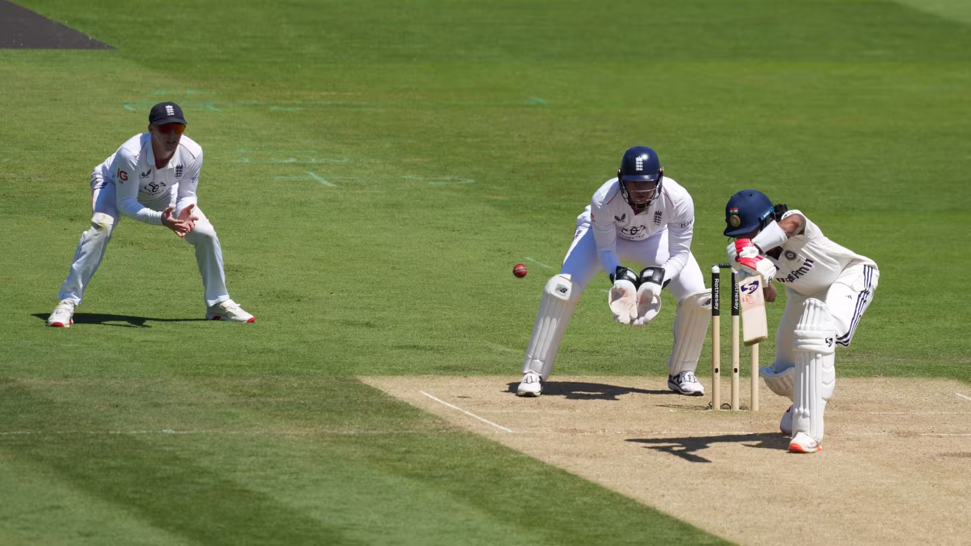 Close-up Test match action at Lord's: an Indian batsman plays a defensive shot as the England wicketkeeper crouches to collect and a slip fielder waits, with the green outfield stretching behind