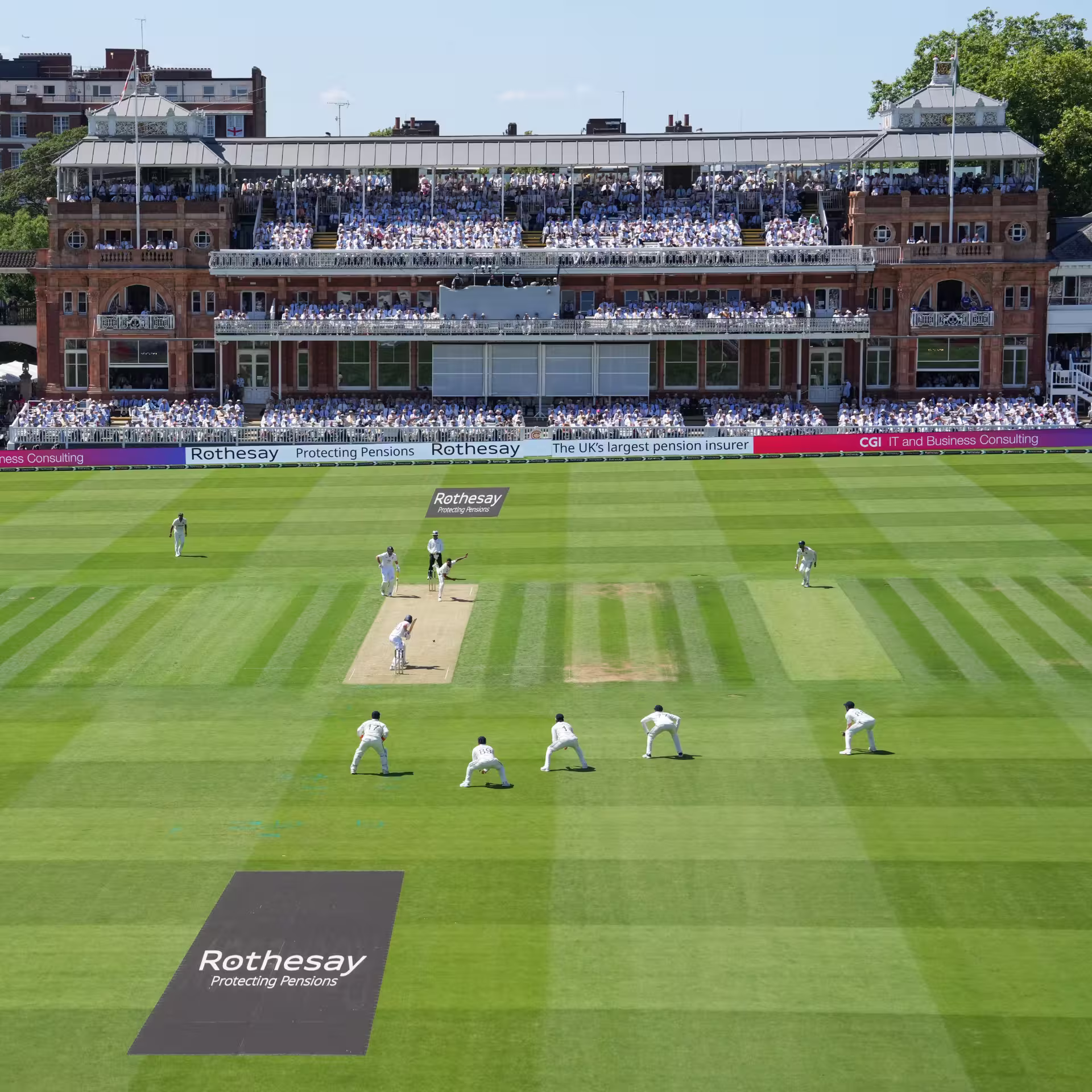 Wide view of a Test match between England and India at Lord's, with India bowling to England's Root and Pope, the iconic Victorian pavilion packed with spectators, and the scoreboard visible on the left