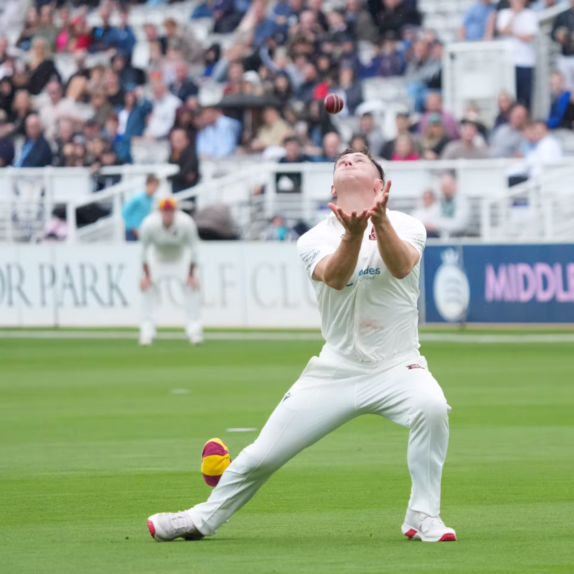 Fielder in cricket whites positioning to take a catch at Lord's, with Middlesex Members' advertising boards and spectators in the background