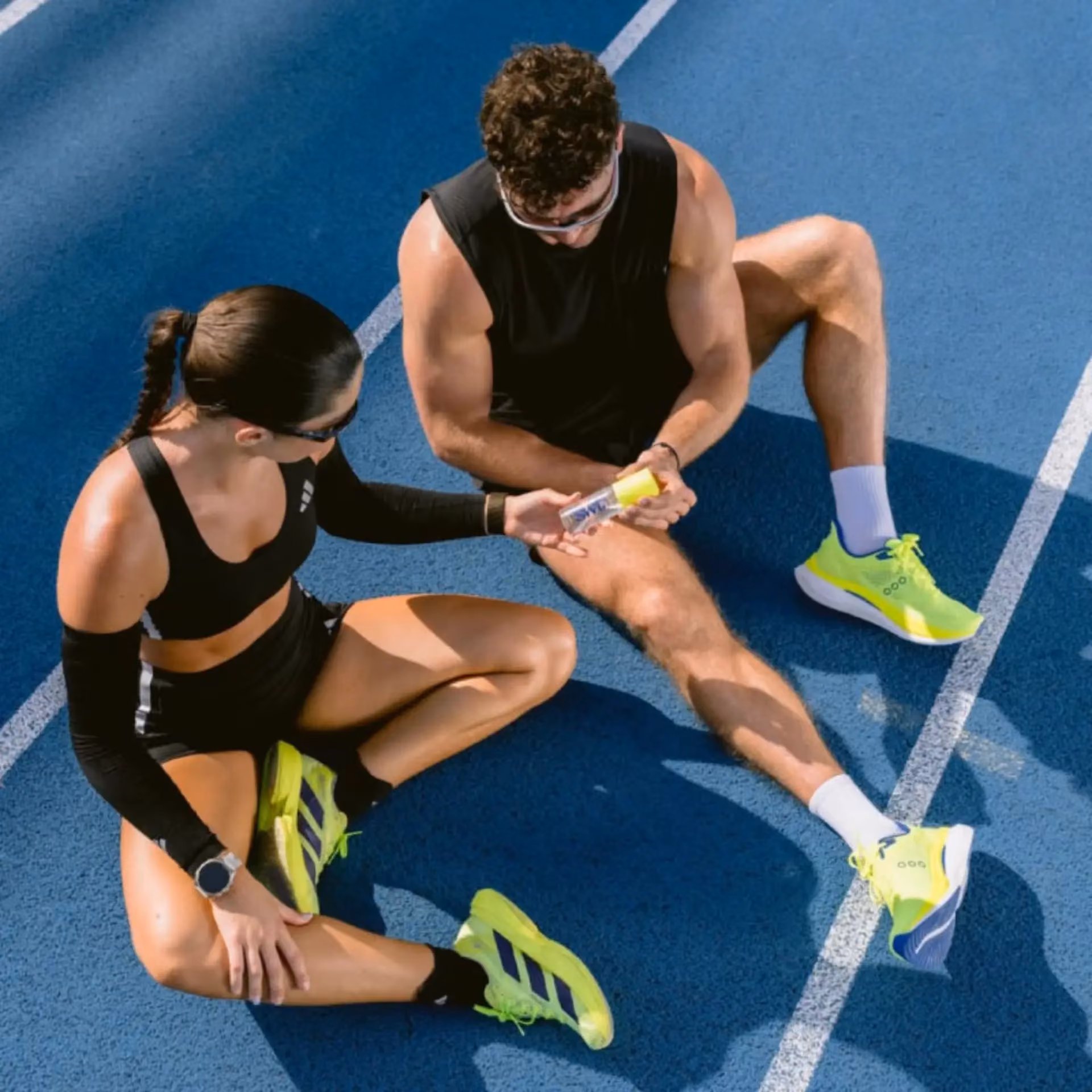 A man and woman sit on the ground, both wearing shoes, enjoying a casual moment together.