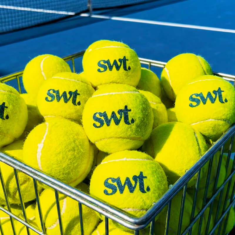 A basket filled with SWT tennis balls, showcasing their bright yellow color and distinctive logo.