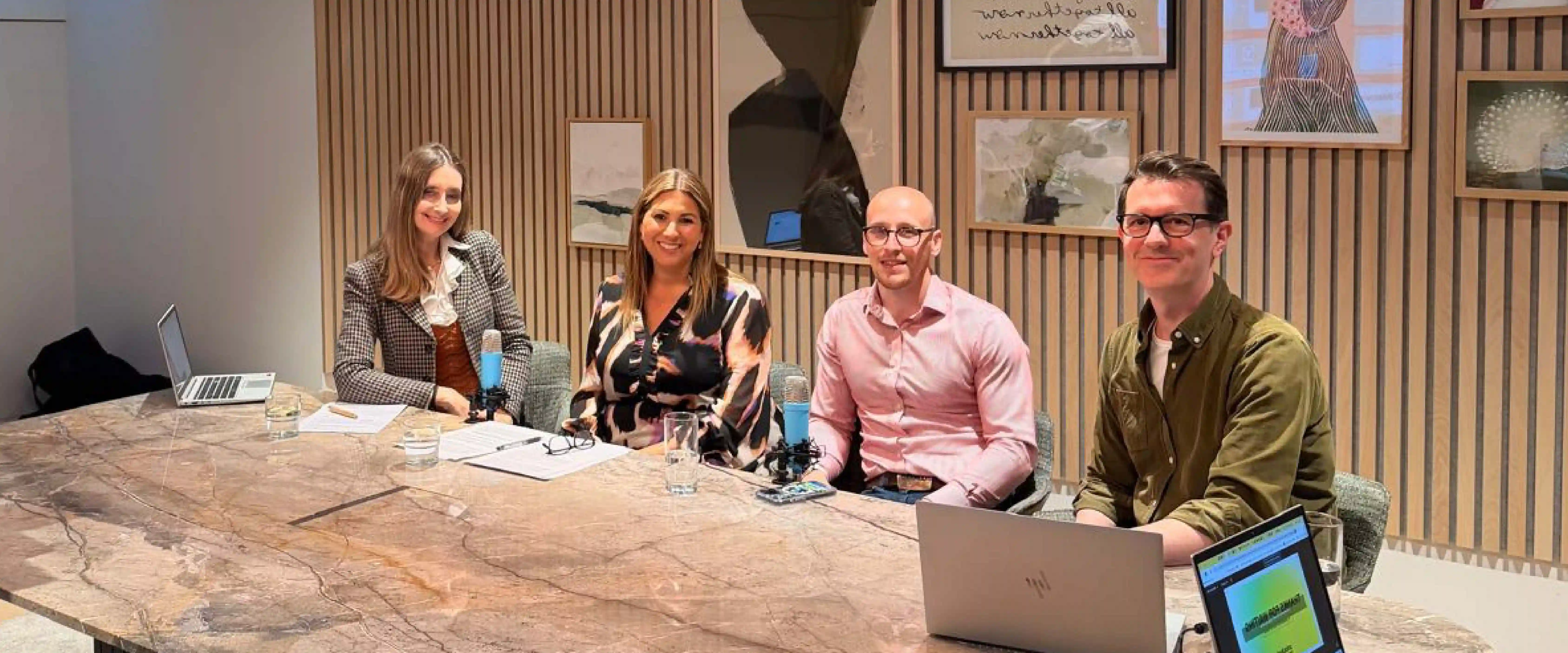 Group of four professionals sitting around a large conference table for a webinar recording