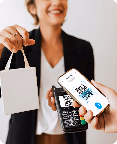 Person holding a small white shopping bag while another hand scans a QR code on a smartphone using a card reader.