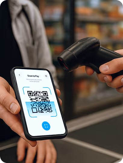 Person scanning a QR code displayed on a smartphone screen using a handheld barcode scanner at a checkout counter.