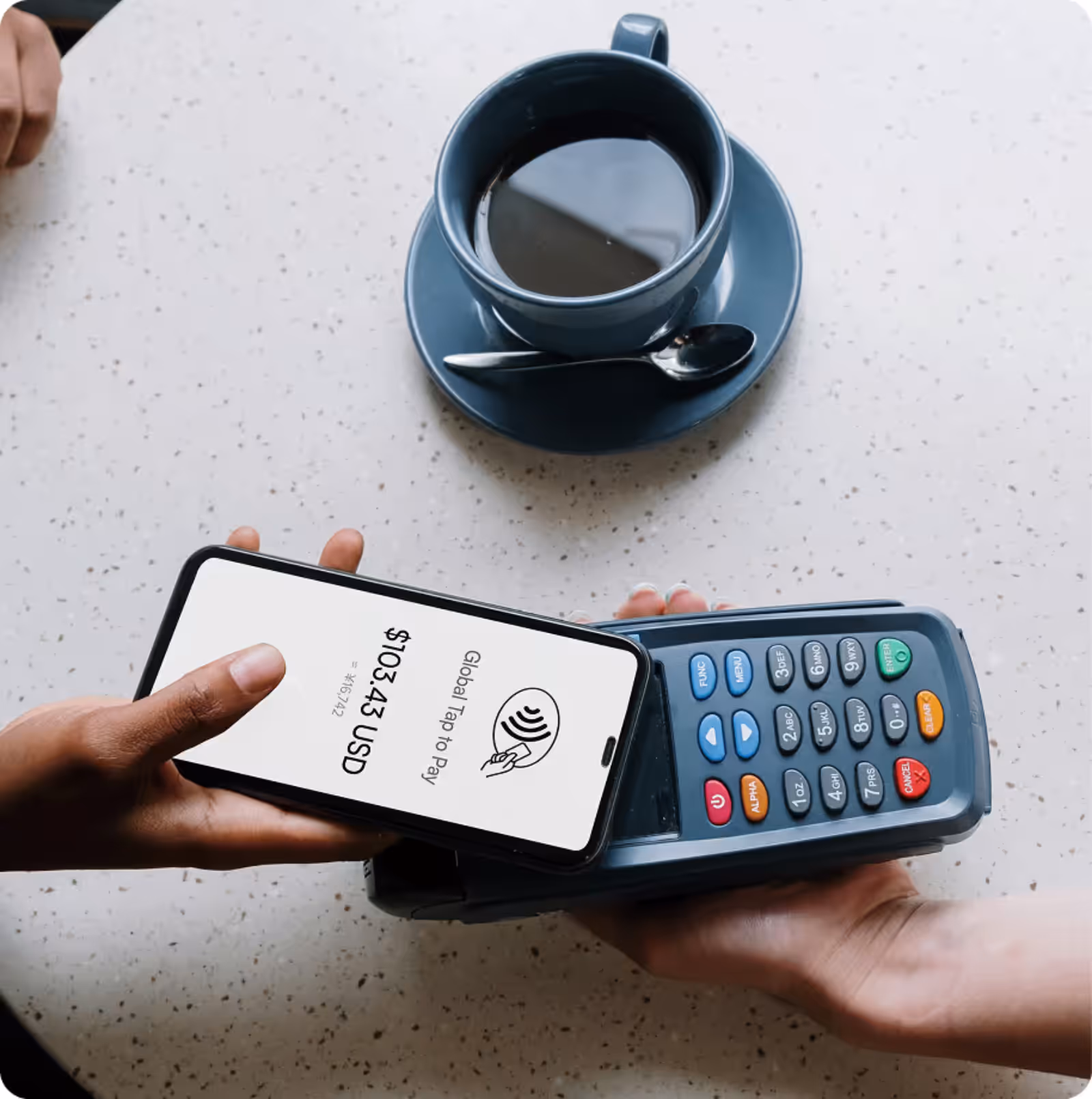 Person making a contactless payment with a smartphone on a card reader while a cup of coffee sits on a table.