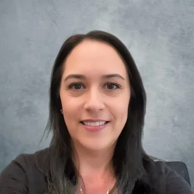 Woman with long dark hair smiling in front of a gray textured background.