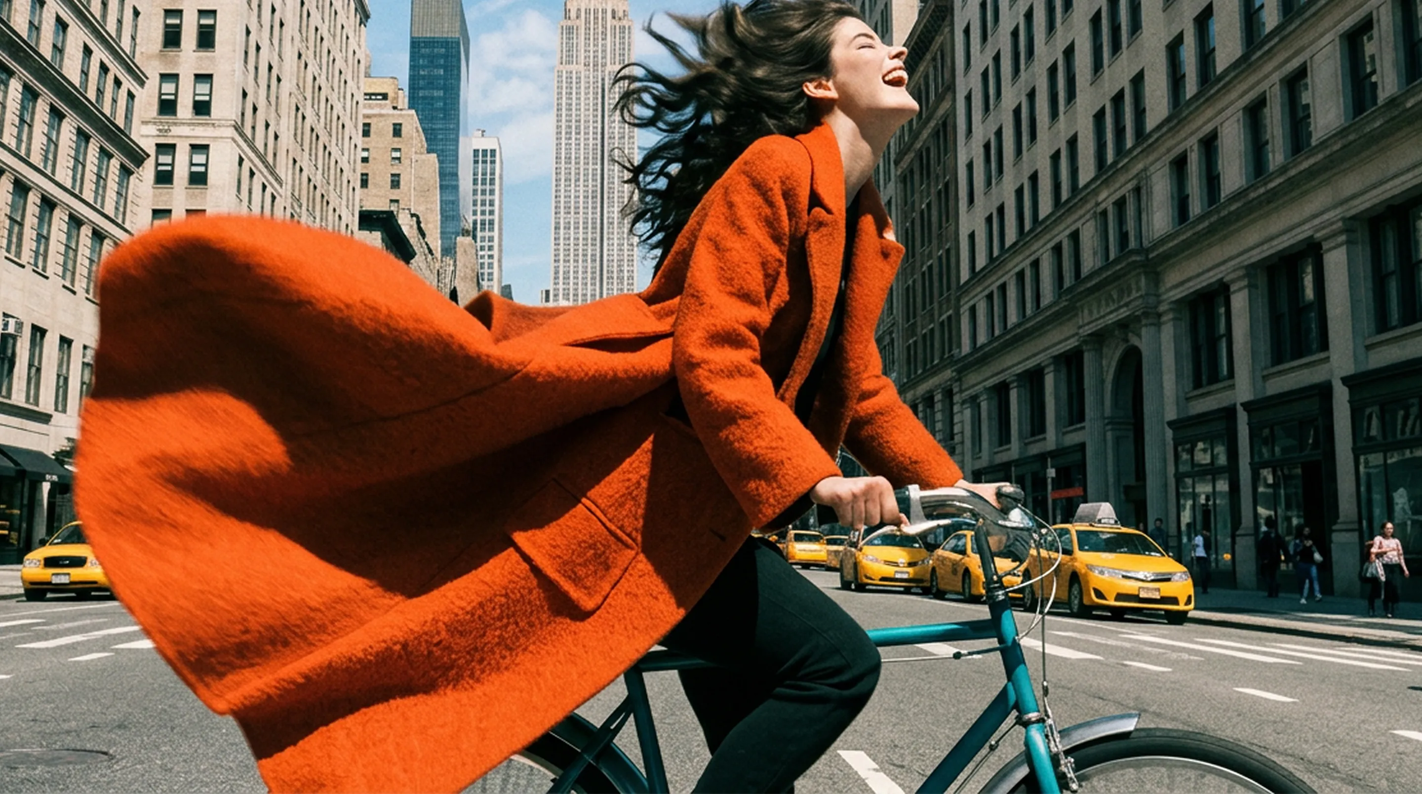 A woman wearing a vibrant orange textured coat riding a vintage bicycle in NYC.