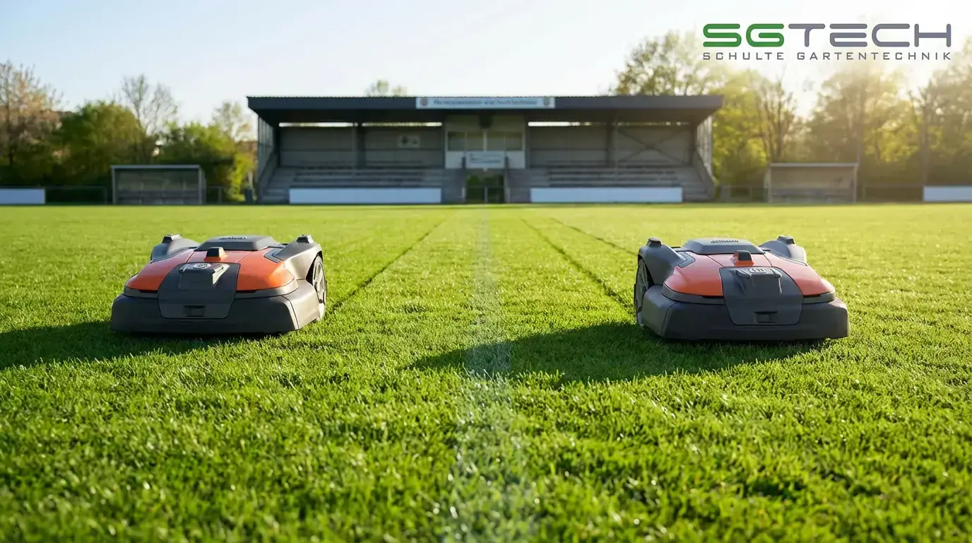 Zwei Husqvarna 580 EPOS Rasenroboter mähen ein Fussballfeld im Frühling, mit Tribüne im Hintergrund.