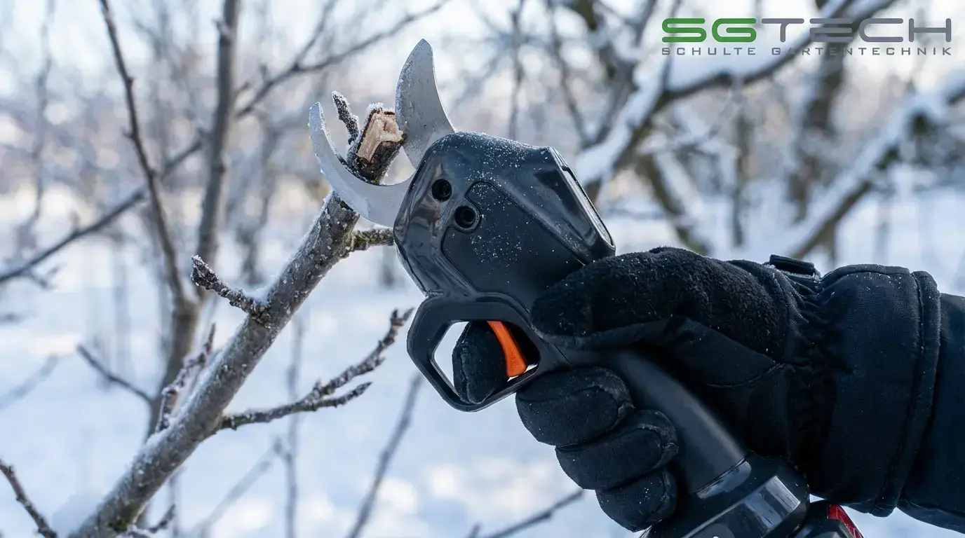 Hand im Winterhandschuh hält schwarze Akku-Astschere mit orangefarbenem Abzug, bereit zum Schneiden eines Astes im Schnee.